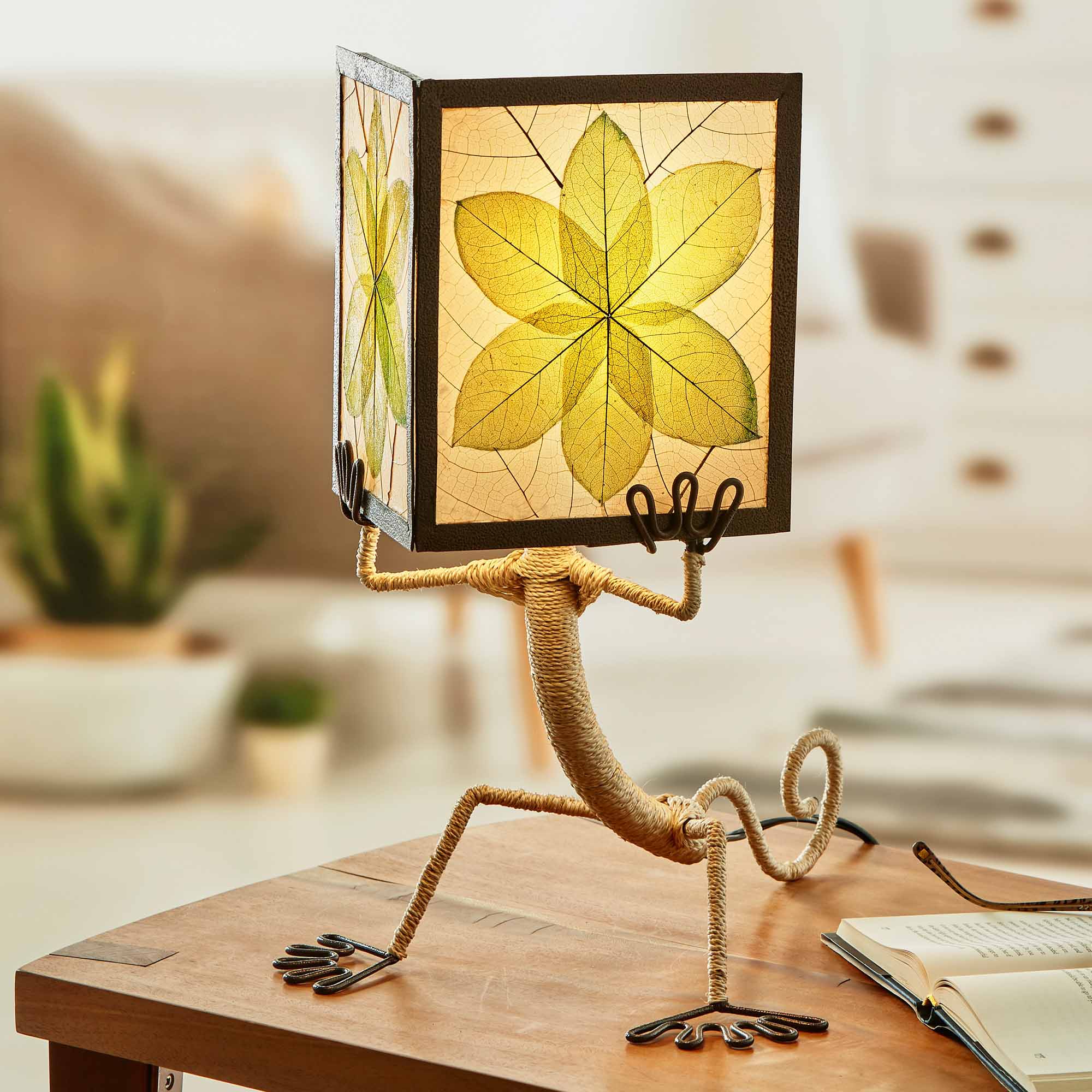 In a modern interior with earth tones, crafted by the artisans of Eangee Home Design, the Enlightened Gecko Table Lamp in green stands gracefully, featuring fossilized cocoa leaf shade, guyabano leaf shade, abaca rope accents, wrought iron frame, handcrafted, adding warmth and character to the space.