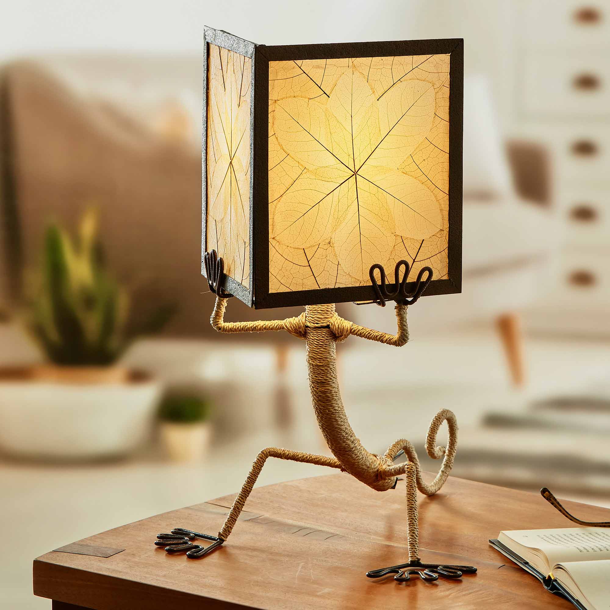 In a coastal inspired living room, crafted by the artisans of Eangee Home Design, the Enlightened Gecko Table Lamp in natural stands gracefully, featuring fossilized cocoa leaf shade, guyabano leaf shade, abaca rope accents, wrought iron frame, handcrafted, adding warmth and character to the space.