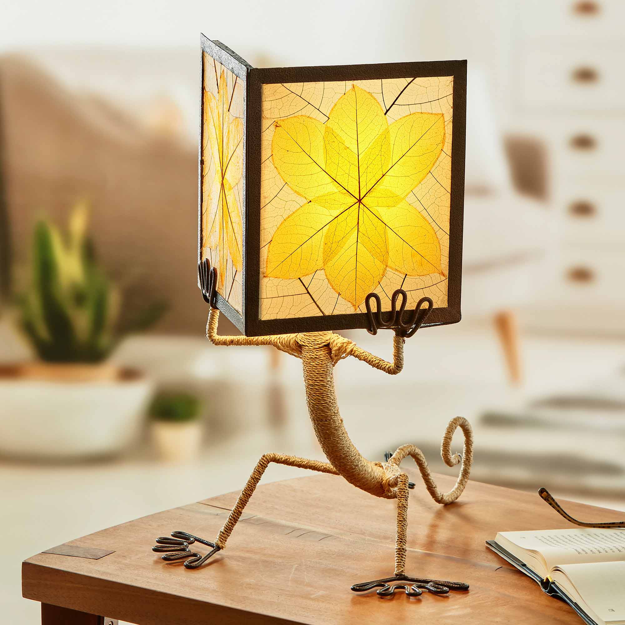 In a sun drenched entryway, crafted by the artisans of Eangee Home Design, the Enlightened Gecko Table Lamp in orange stands gracefully, featuring fossilized cocoa leaf shade, guyabano leaf shade, abaca rope accents, wrought iron frame, handcrafted, adding warmth and character to the space.