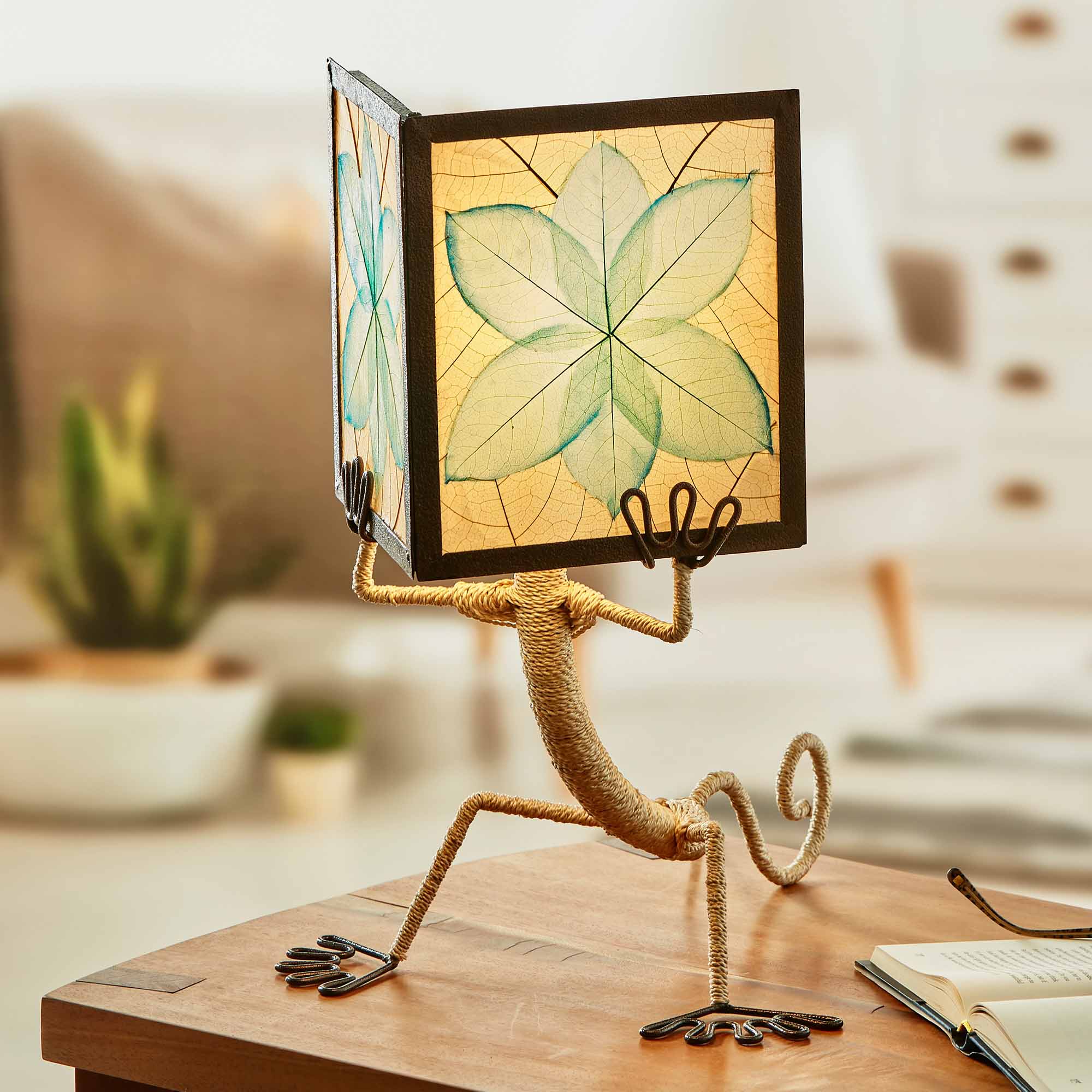 In a quiet bedside corner, crafted by the artisans of Eangee Home Design, the Enlightened Gecko Table Lamp in sea blue stands gracefully, featuring fossilized cocoa leaf shade, guyabano leaf shade, abaca rope accents, wrought iron frame, handcrafted, adding warmth and character to the space.