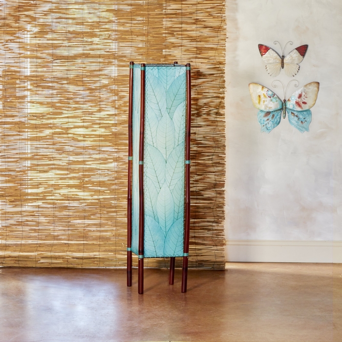In a minimalist loft with natural textures, crafted by the artisans of Eangee Home Design, the Fortune Large Floor Lamp in sea blue stands gracefully, featuring fossilized cocoa leaf shade, abaca rope accents, rattan leg supports, wrought iron frame, handcrafted, adding warmth and character to the space.