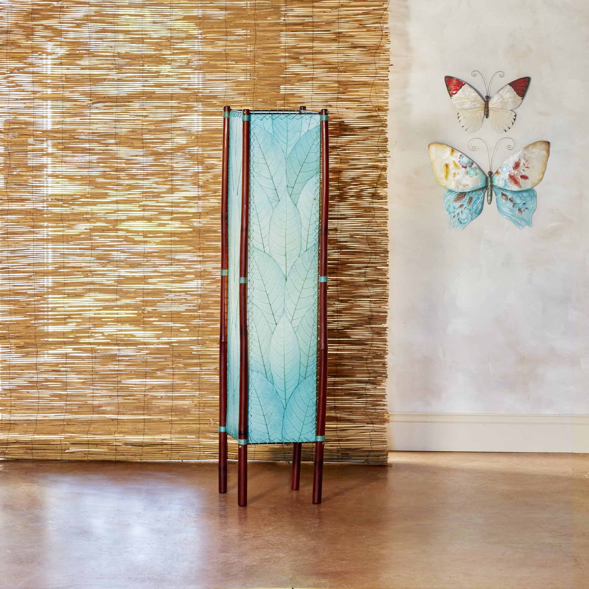 In a minimalist loft with natural textures, crafted by the artisans of Eangee Home Design, the Fortune Large Floor Lamp in sea blue stands gracefully, featuring fossilized cocoa leaf shade, abaca rope accents, rattan leg supports, wrought iron frame, handcrafted, adding warmth and character to the space.
