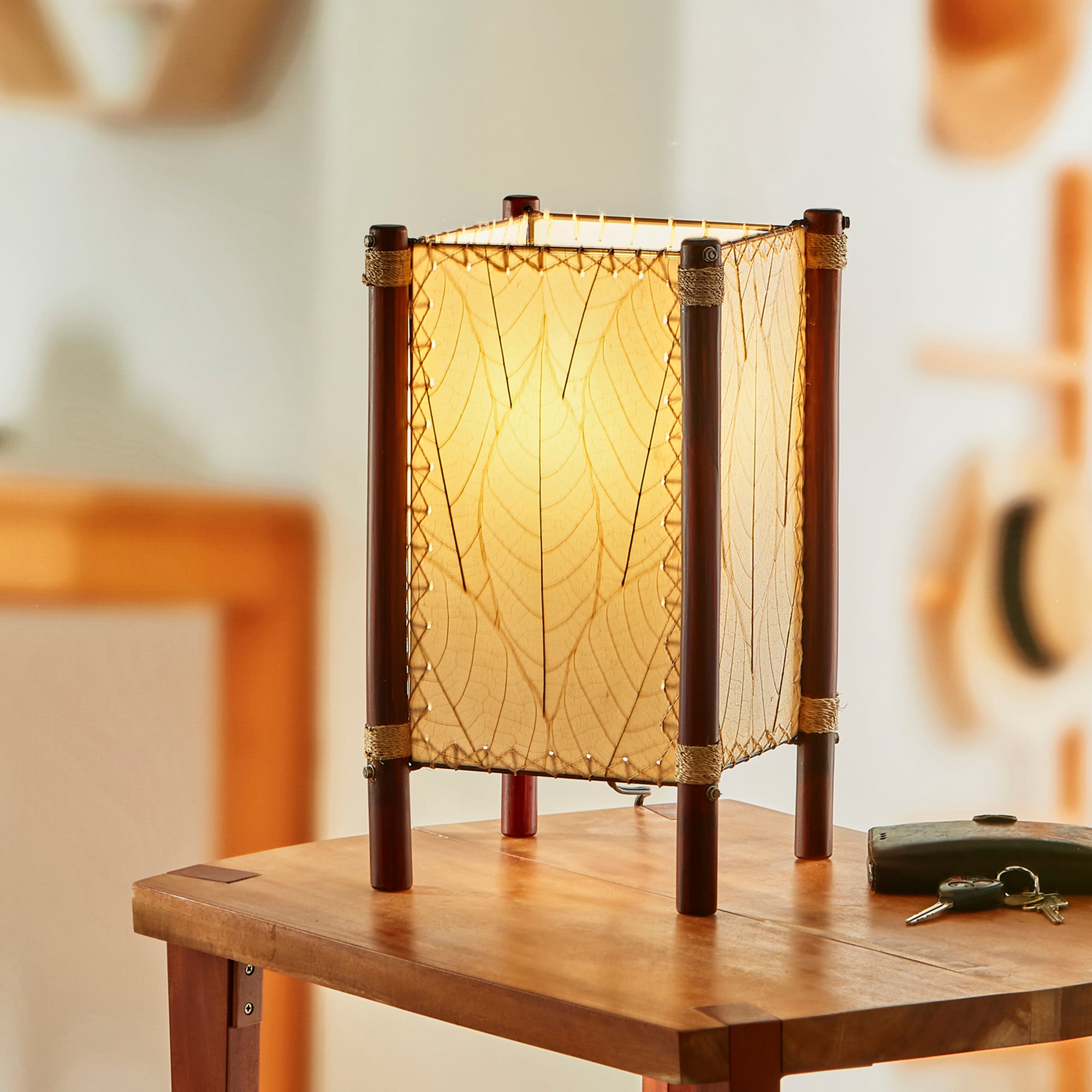 In a quiet bedside corner, crafted by the artisans of Eangee Home Design, the Fortune Table Lamp in natural stands gracefully, featuring fossilized cocoa leaf shade, abaca rope accents, rattan leg supports, adding warmth and character to the space.