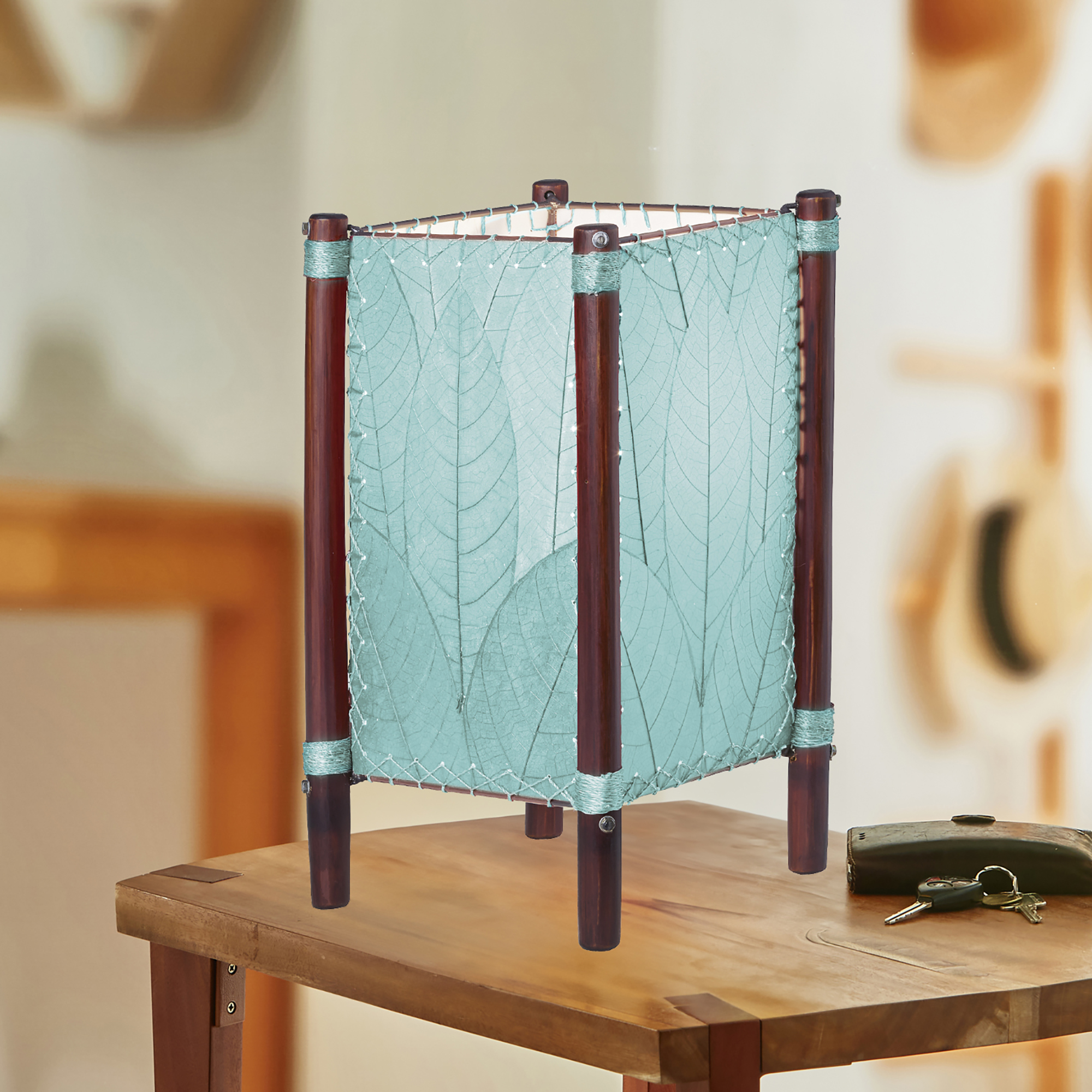 In a modern interior with earth tones, crafted by the artisans of Eangee Home Design, the Fortune Table Lamp in sea blue stands gracefully, featuring fossilized cocoa leaf shade, abaca rope accents, rattan leg supports, adding warmth and character to the space.