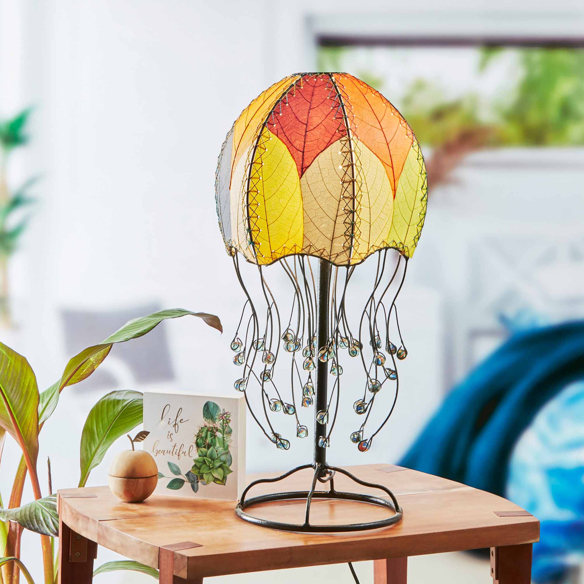 In a modern interior with earth tones, crafted by the artisans of Eangee Home Design, the Jellyfish Table Lamp in multi color stands gracefully, featuring fossilized cocoa leaf shade, abaca rope accents, wrought iron frame, handcrafted, adding warmth and character to the space.