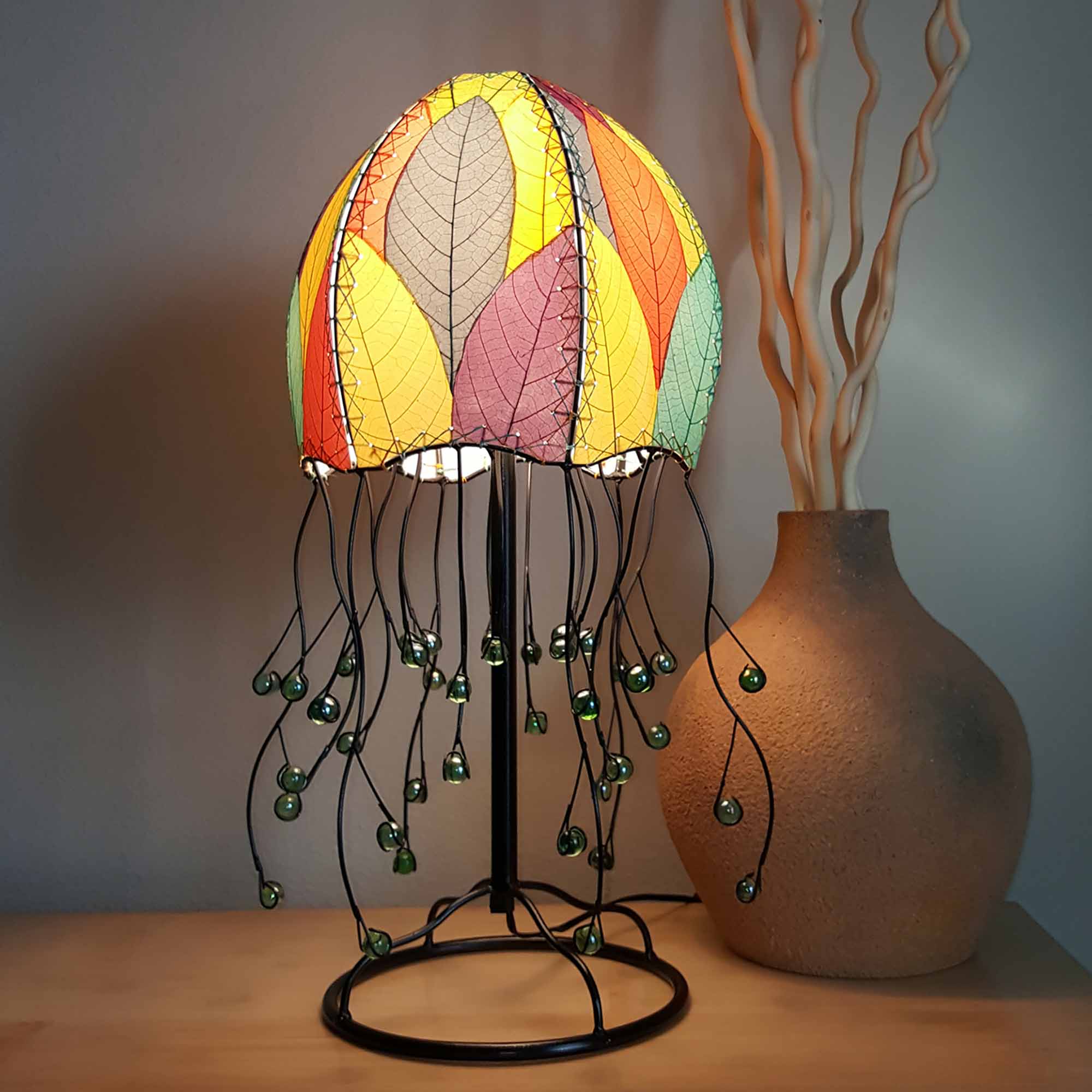 In a coastal inspired living room, crafted by the artisans of Eangee Home Design, the Jellyfish Table Lamp in multi color stands gracefully, featuring fossilized cocoa leaf shade, abaca rope accents, wrought iron frame, handcrafted, adding warmth and character to the space.