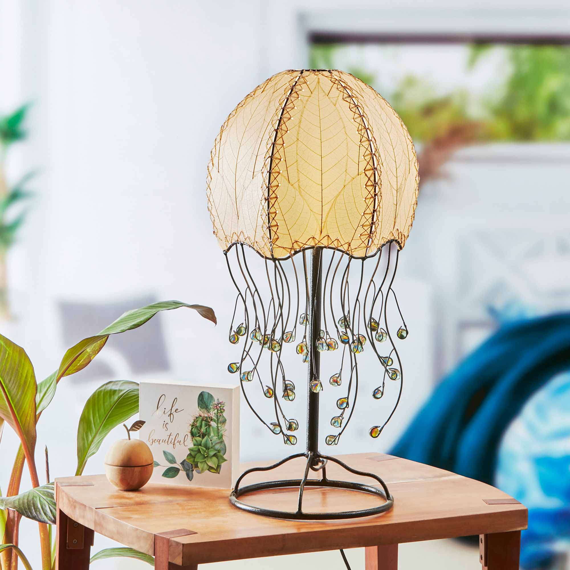 In a minimalist loft with natural textures, crafted by the artisans of Eangee Home Design, the Jellyfish Table Lamp in natural stands gracefully, featuring fossilized cocoa leaf shade, abaca rope accents, wrought iron frame, handcrafted, adding warmth and character to the space.