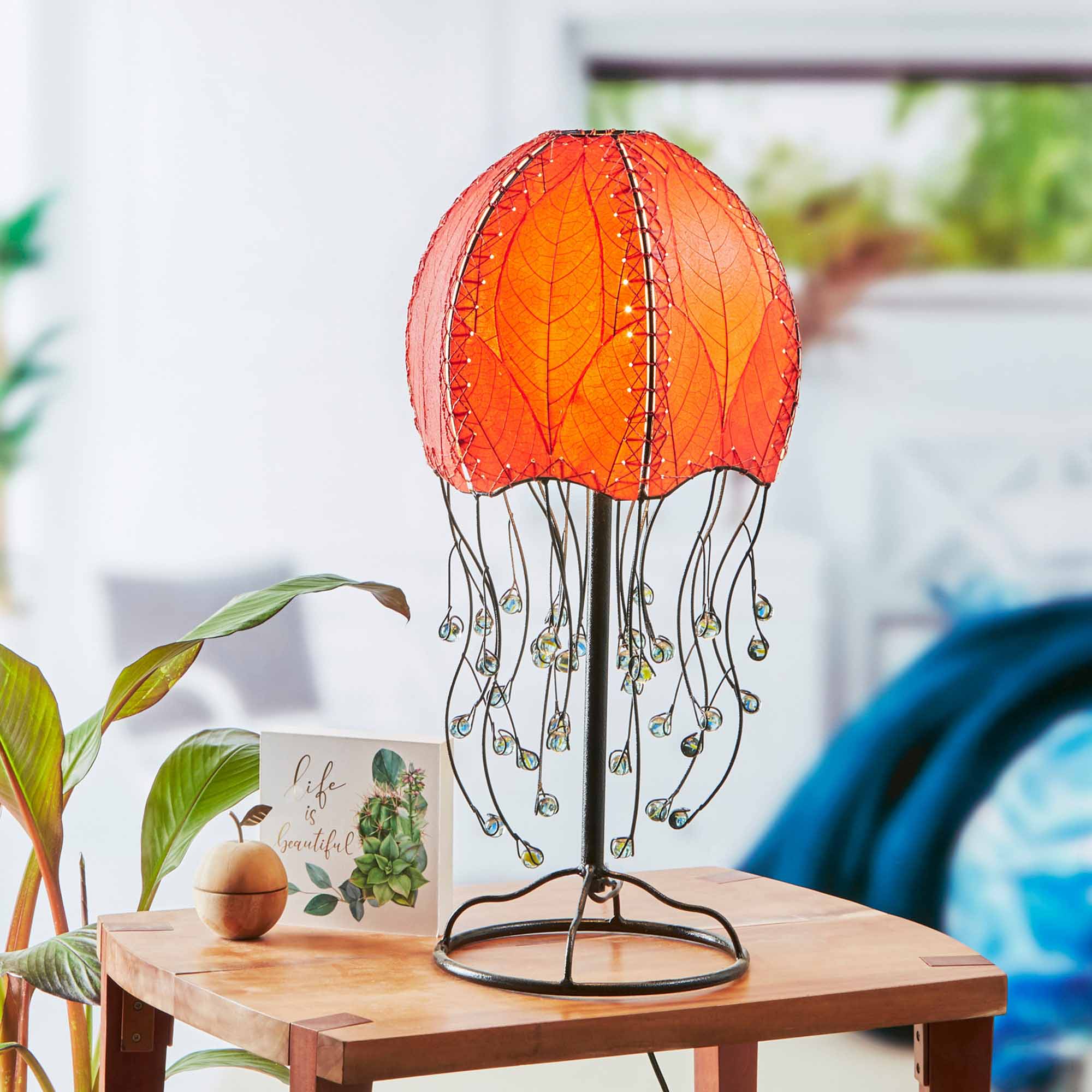 In a coastal inspired living room, crafted by the artisans of Eangee Home Design, the Jellyfish Table Lamp in red stands gracefully, featuring fossilized cocoa leaf shade, abaca rope accents, wrought iron frame, handcrafted, adding warmth and character to the space.