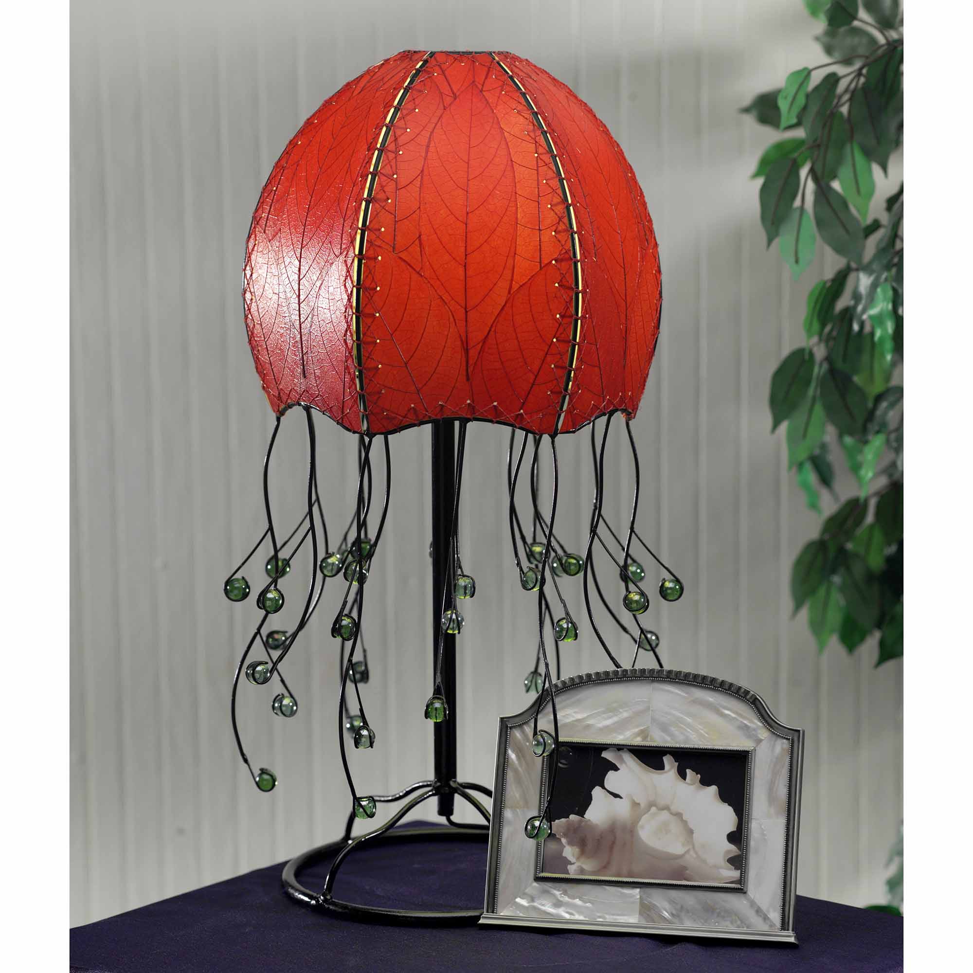 In a modern interior with earth tones, crafted by the artisans of Eangee Home Design, the Jellyfish Table Lamp in red stands gracefully, featuring fossilized cocoa leaf shade, abaca rope accents, wrought iron frame, handcrafted, adding warmth and character to the space.