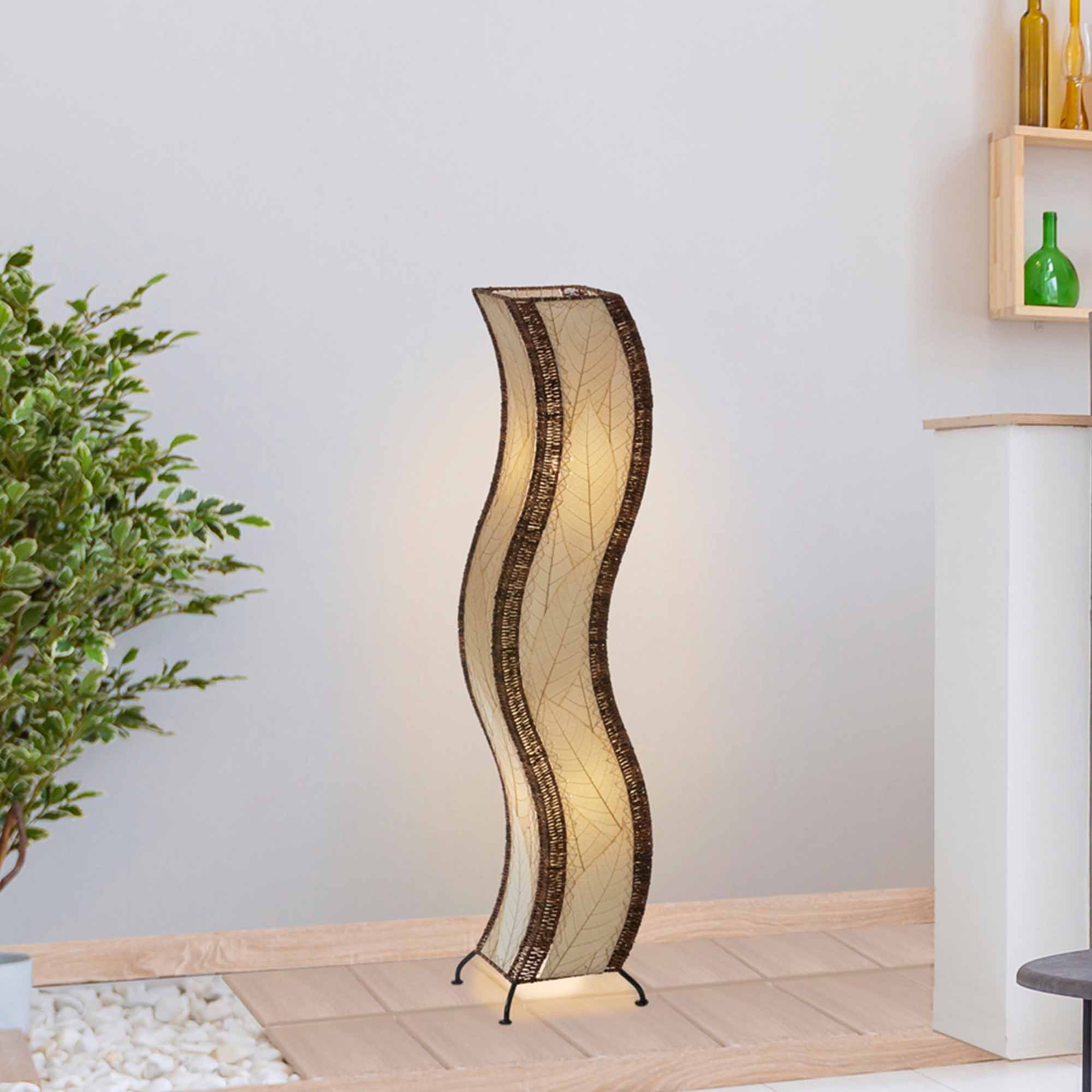 In a modern interior with earth tones, crafted by the artisans of Eangee Home Design, the Wave Large Floor Lamp in natural stands gracefully, featuring fossilized cocoa leaf shade, abaca rope accents, handcrafted, adding warmth and character to the space.