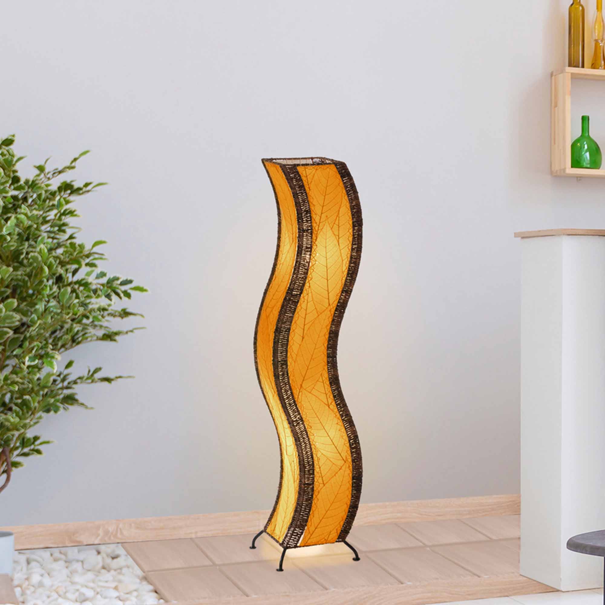 In a softly lit reading nook, crafted by the artisans of Eangee Home Design, the Wave Large Floor Lamp in orange stands gracefully, featuring fossilized cocoa leaf shade, abaca rope accents, handcrafted, adding warmth and character to the space.