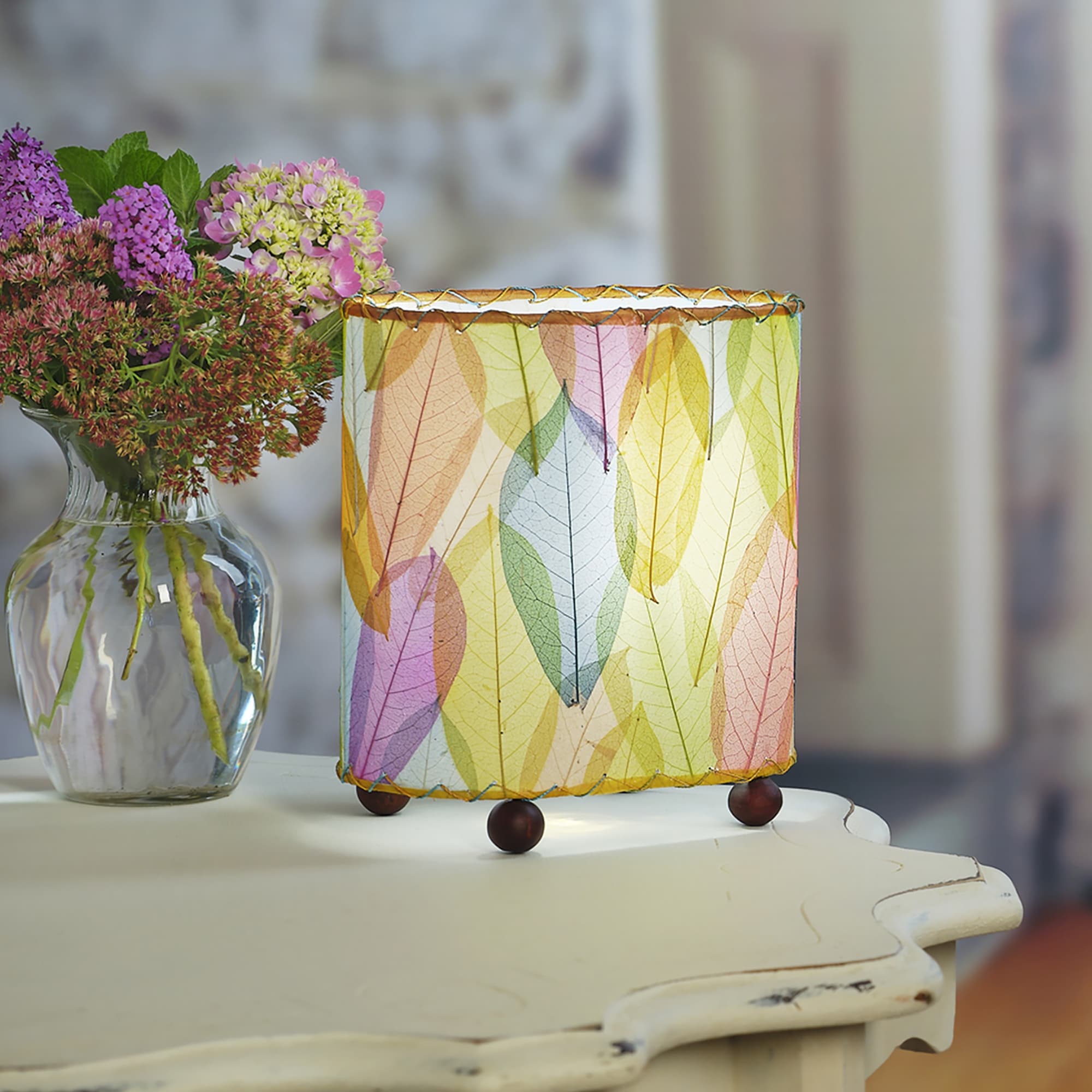 Crafted by the artisans of Eangee Home Design, the Mini Guyabano Table Lamp in multi color against a clean backdrop, featuring fossilized cocoa leaf shade, guyabano leaf shade, wrought iron frame.
