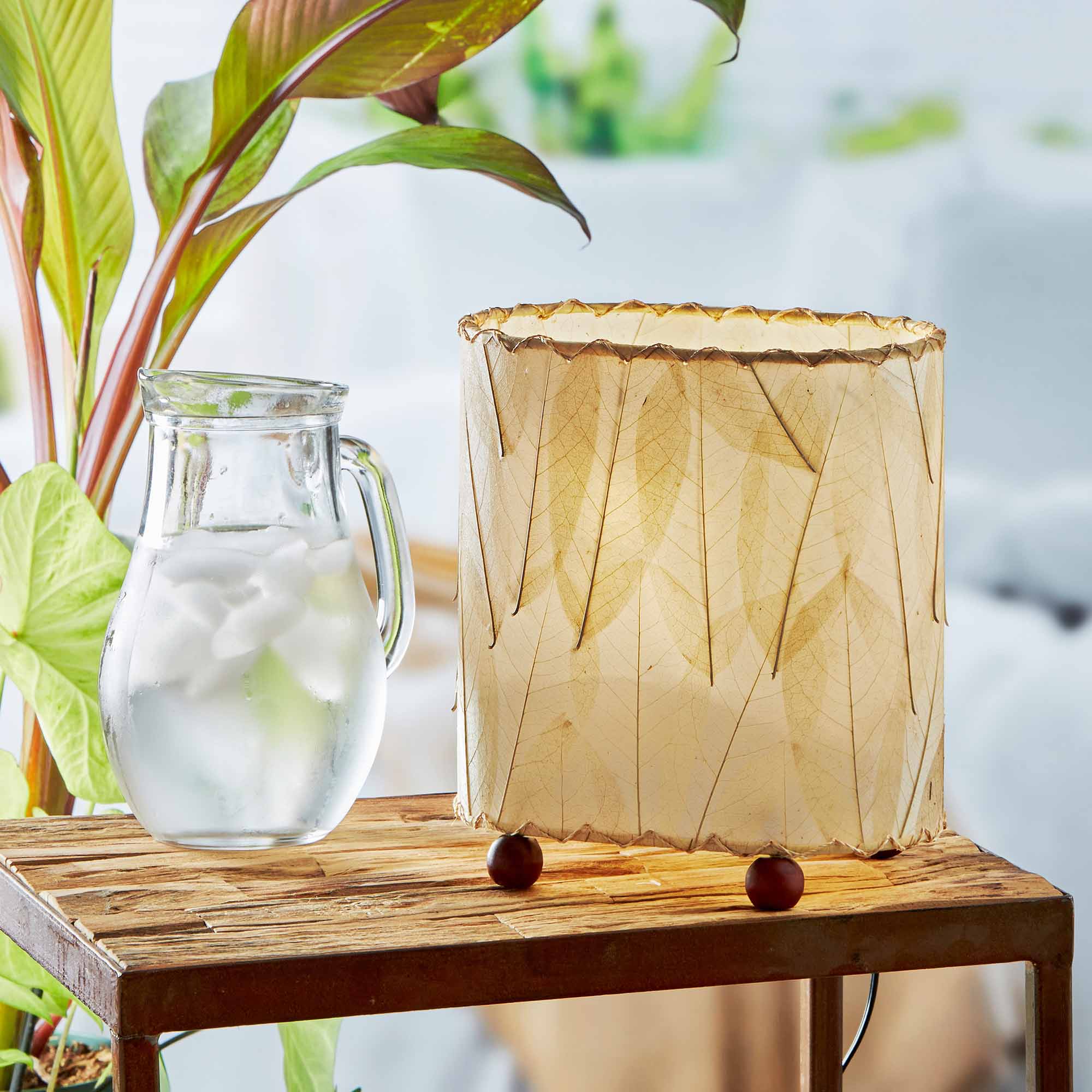 In a softly lit reading nook, crafted by the artisans of Eangee Home Design, the Mini Guyabano Table Lamp in natural stands gracefully, featuring fossilized cocoa leaf shade, guyabano leaf shade, wrought iron frame, adding warmth and character to the space.