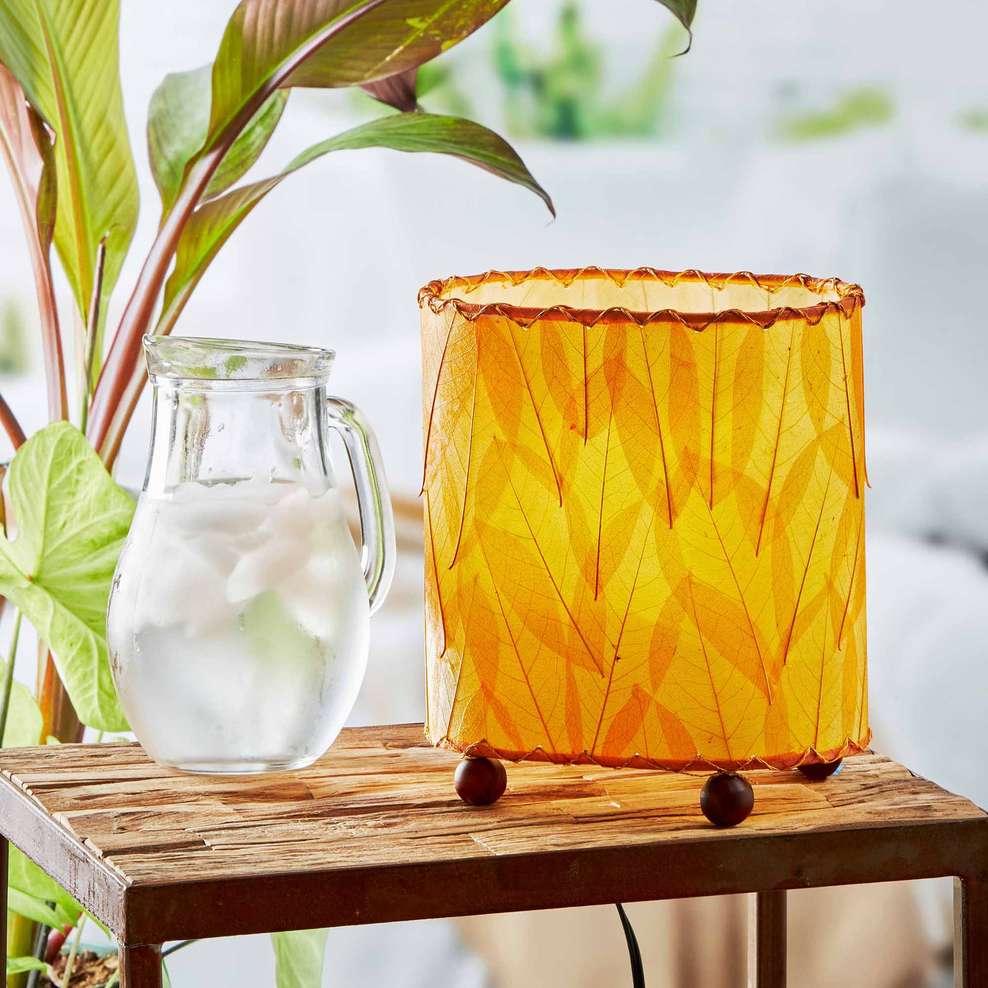 In a coastal inspired living room, crafted by the artisans of Eangee Home Design, the Mini Guyabano Table Lamp in orange stands gracefully, featuring fossilized cocoa leaf shade, guyabano leaf shade, wrought iron frame, adding warmth and character to the space.
