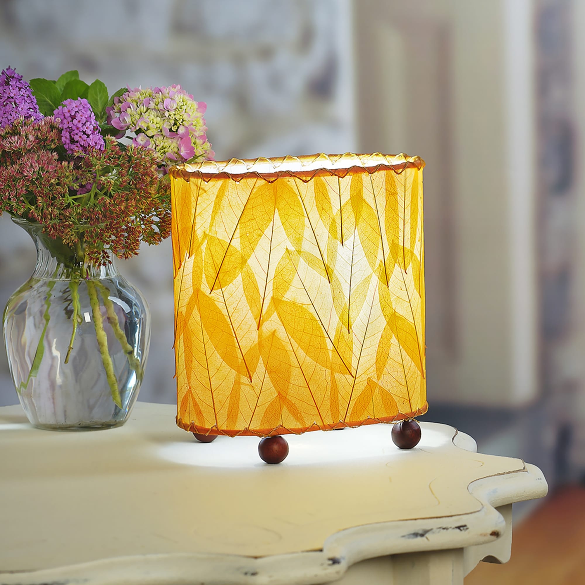 Crafted by the artisans of Eangee Home Design, the Mini Guyabano Table Lamp in orange against a clean backdrop, featuring fossilized cocoa leaf shade, guyabano leaf shade, wrought iron frame.