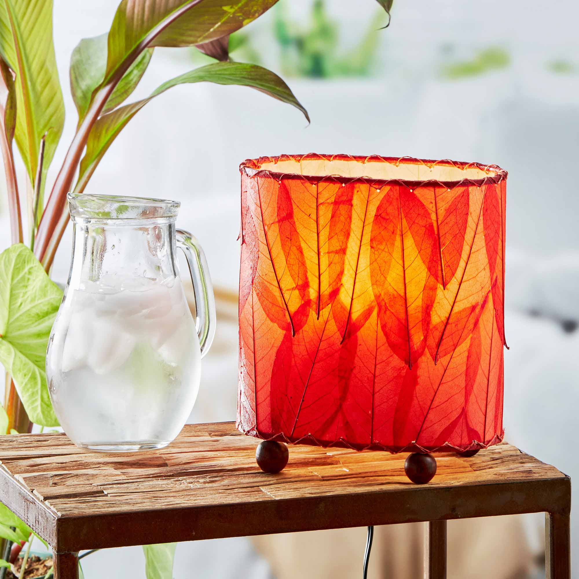In a softly lit reading nook, crafted by the artisans of Eangee Home Design, the Mini Guyabano Table Lamp in red stands gracefully, featuring fossilized cocoa leaf shade, guyabano leaf shade, wrought iron frame, adding warmth and character to the space.