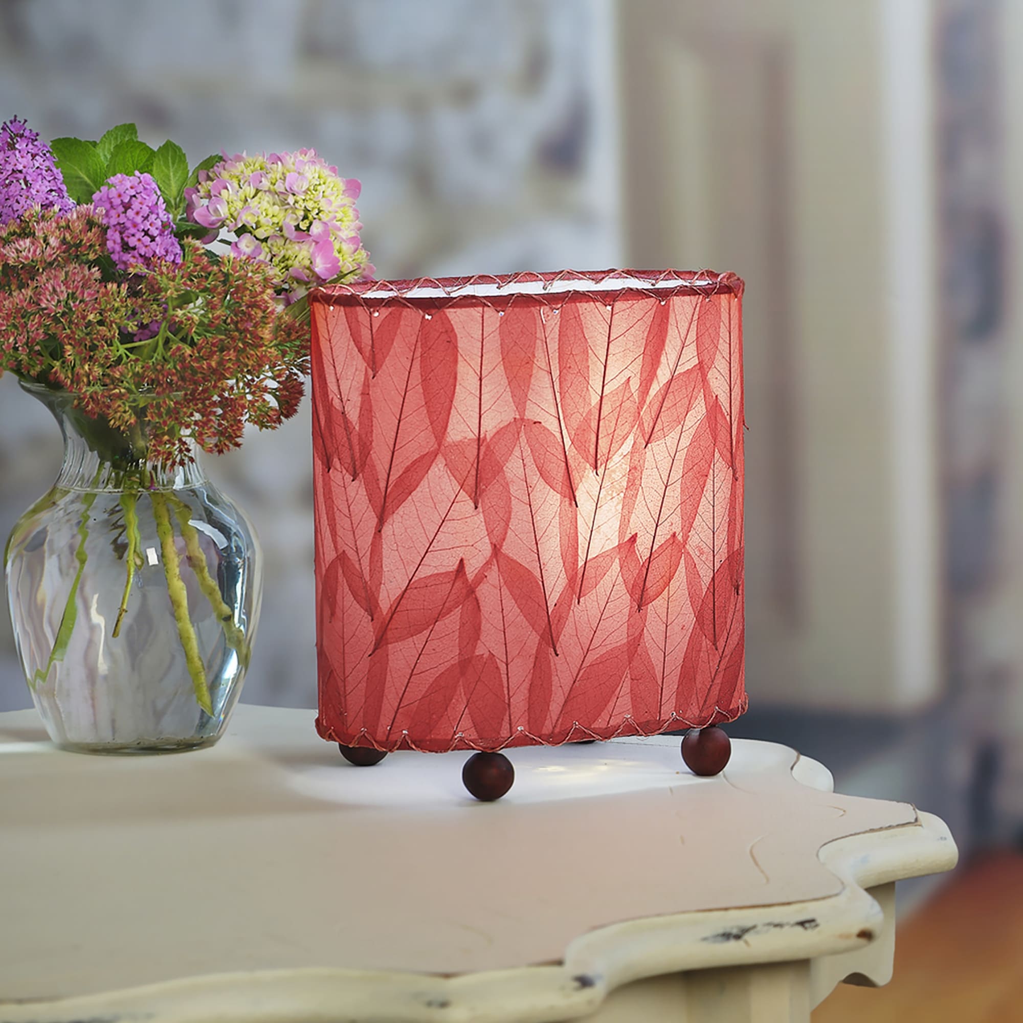 Crafted by the artisans of Eangee Home Design, the Mini Guyabano Table Lamp in red against a clean backdrop, featuring fossilized cocoa leaf shade, guyabano leaf shade, wrought iron frame.