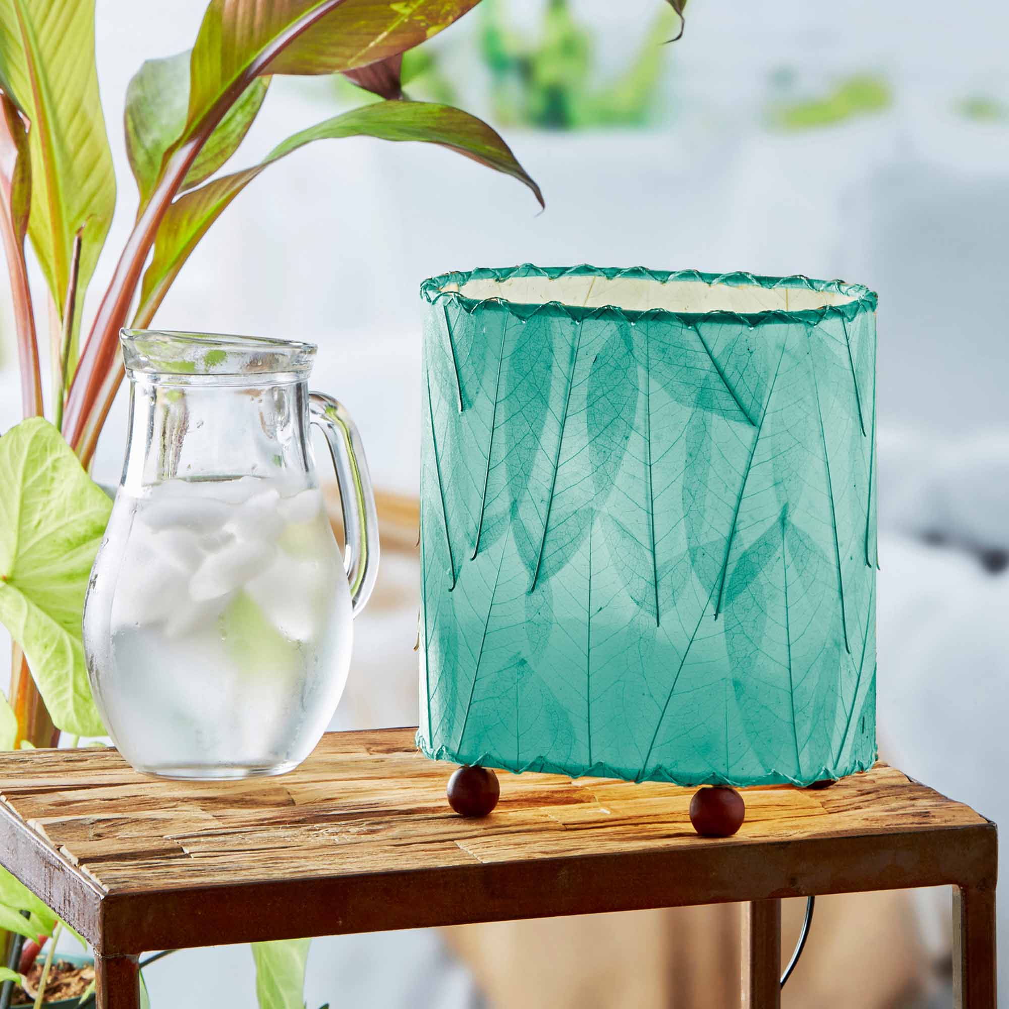 In a sun drenched entryway, crafted by the artisans of Eangee Home Design, the Mini Guyabano Table Lamp in sea blue stands gracefully, featuring fossilized cocoa leaf shade, guyabano leaf shade, wrought iron frame, adding warmth and character to the space.