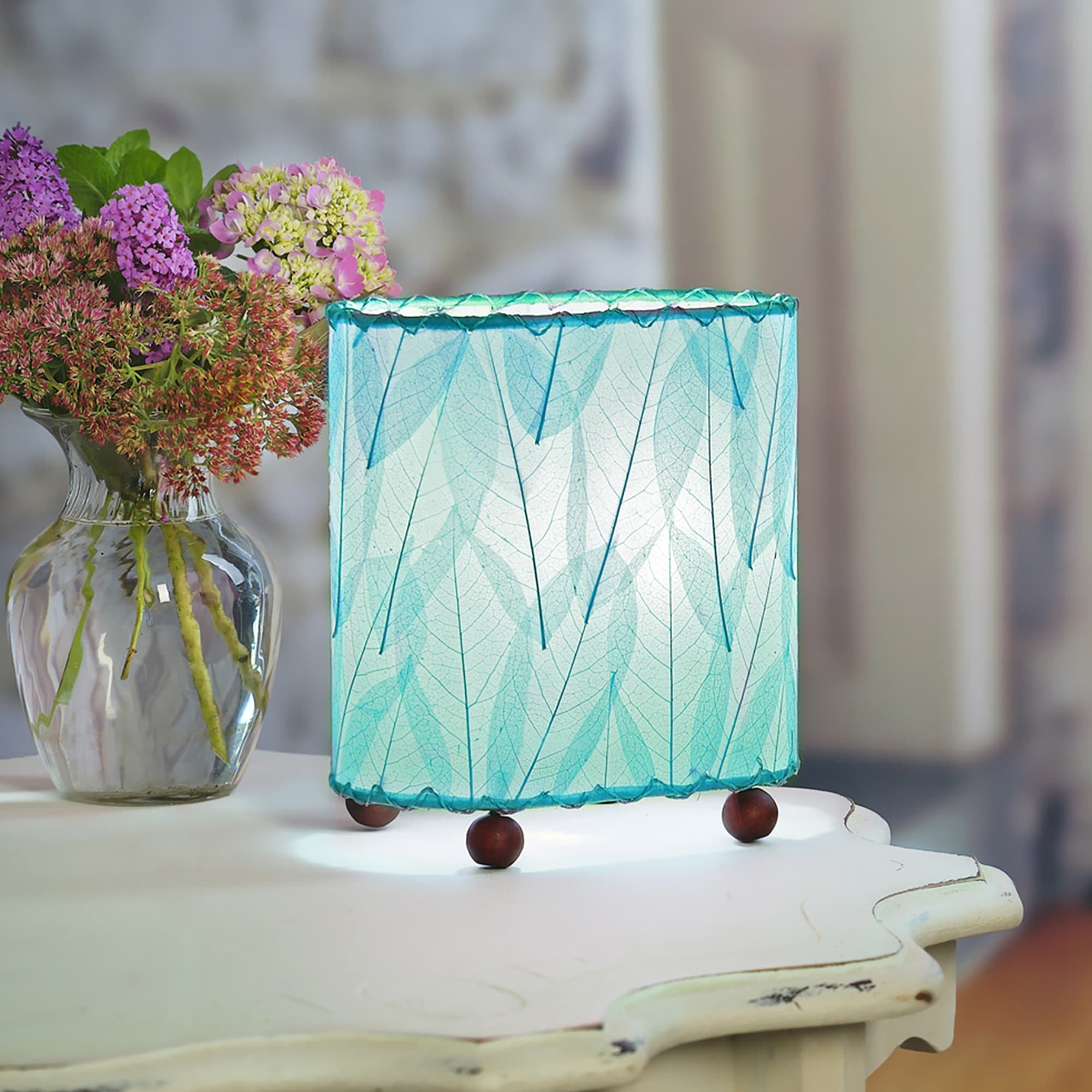 Crafted by the artisans of Eangee Home Design, the Mini Guyabano Table Lamp in sea blue against a clean backdrop, featuring fossilized cocoa leaf shade, guyabano leaf shade, wrought iron frame.