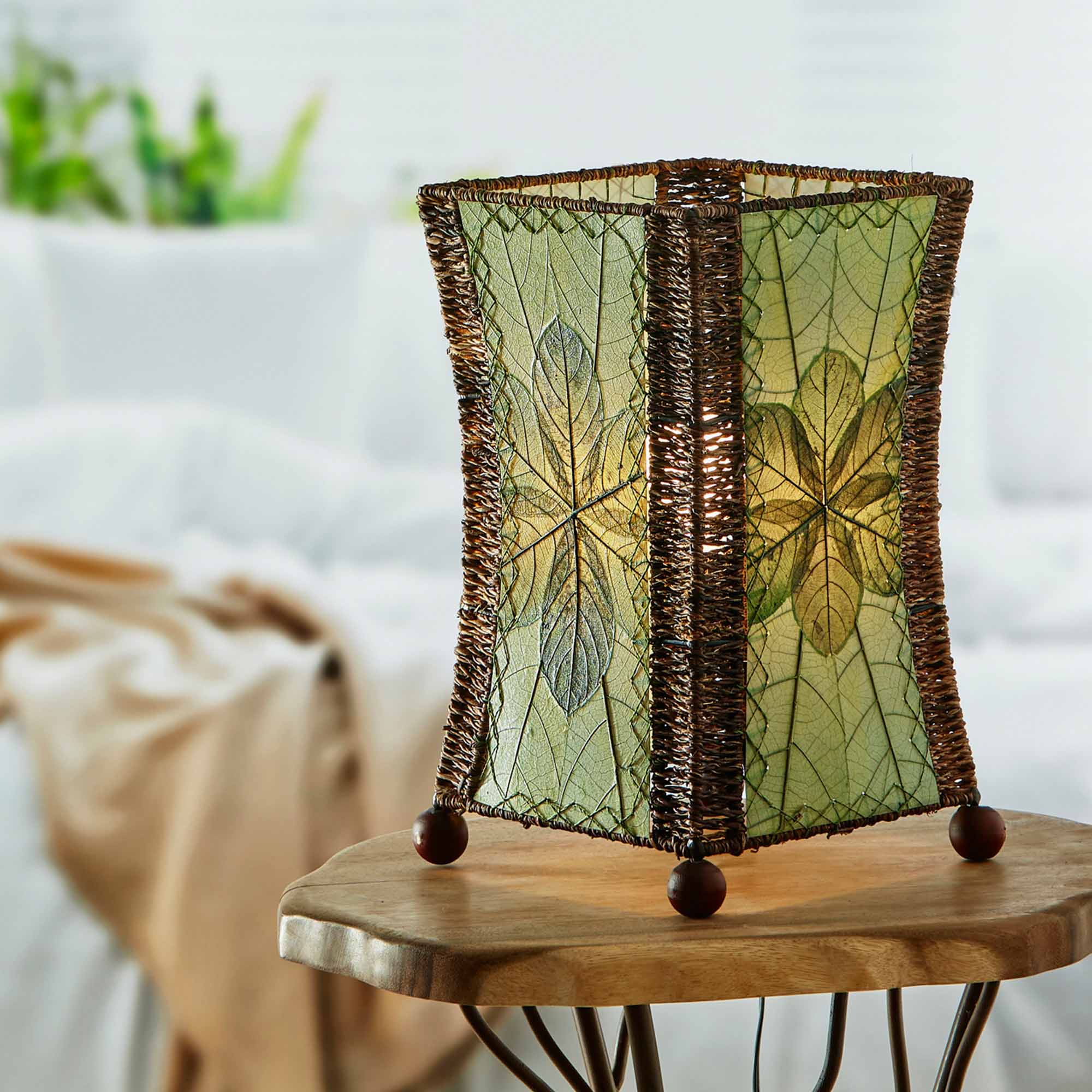 In a coastal inspired living room, crafted by the artisans of Eangee Home Design, the Hourglass Table Lamp in green stands gracefully, featuring jackfruit leaf panels, abaca rope accents, wrought iron frame, eco friendly, adding warmth and character to the space.