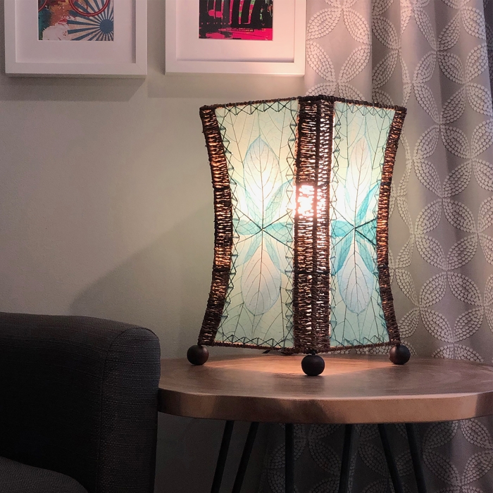 In a coastal inspired living room, crafted by the artisans of Eangee Home Design, the Hourglass Table Lamp in sea blue stands gracefully, featuring jackfruit leaf panels, abaca rope accents, wrought iron frame, eco friendly, adding warmth and character to the space.