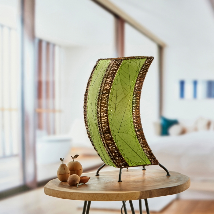 In a quiet bedside corner, crafted by the artisans of Eangee Home Design, the C Shape Table Lamp in green stands gracefully, featuring fossilized cocoa leaf shade, abaca rope accents, fair trade, handcrafted, adding warmth and character to the space.