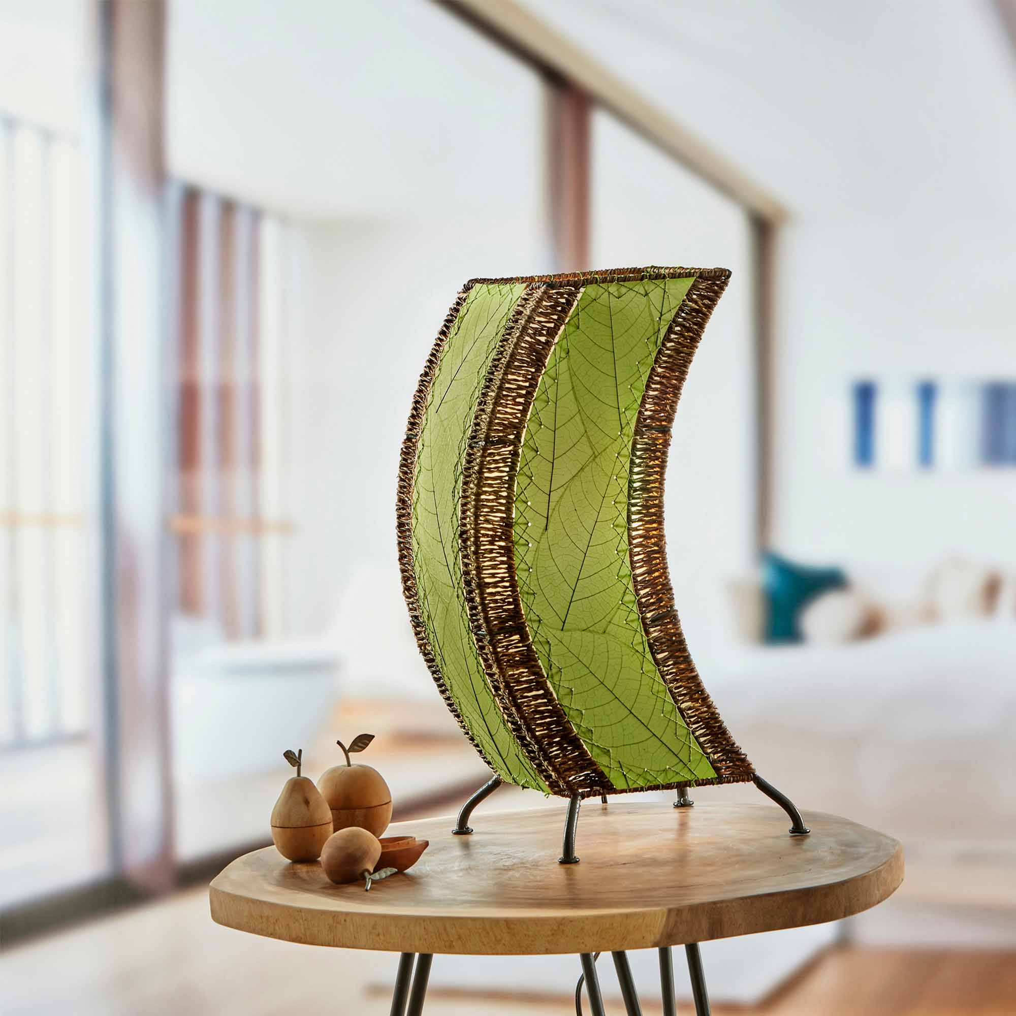 In a quiet bedside corner, crafted by the artisans of Eangee Home Design, the C Shape Table Lamp in green stands gracefully, featuring fossilized cocoa leaf shade, abaca rope accents, fair trade, handcrafted, adding warmth and character to the space.
