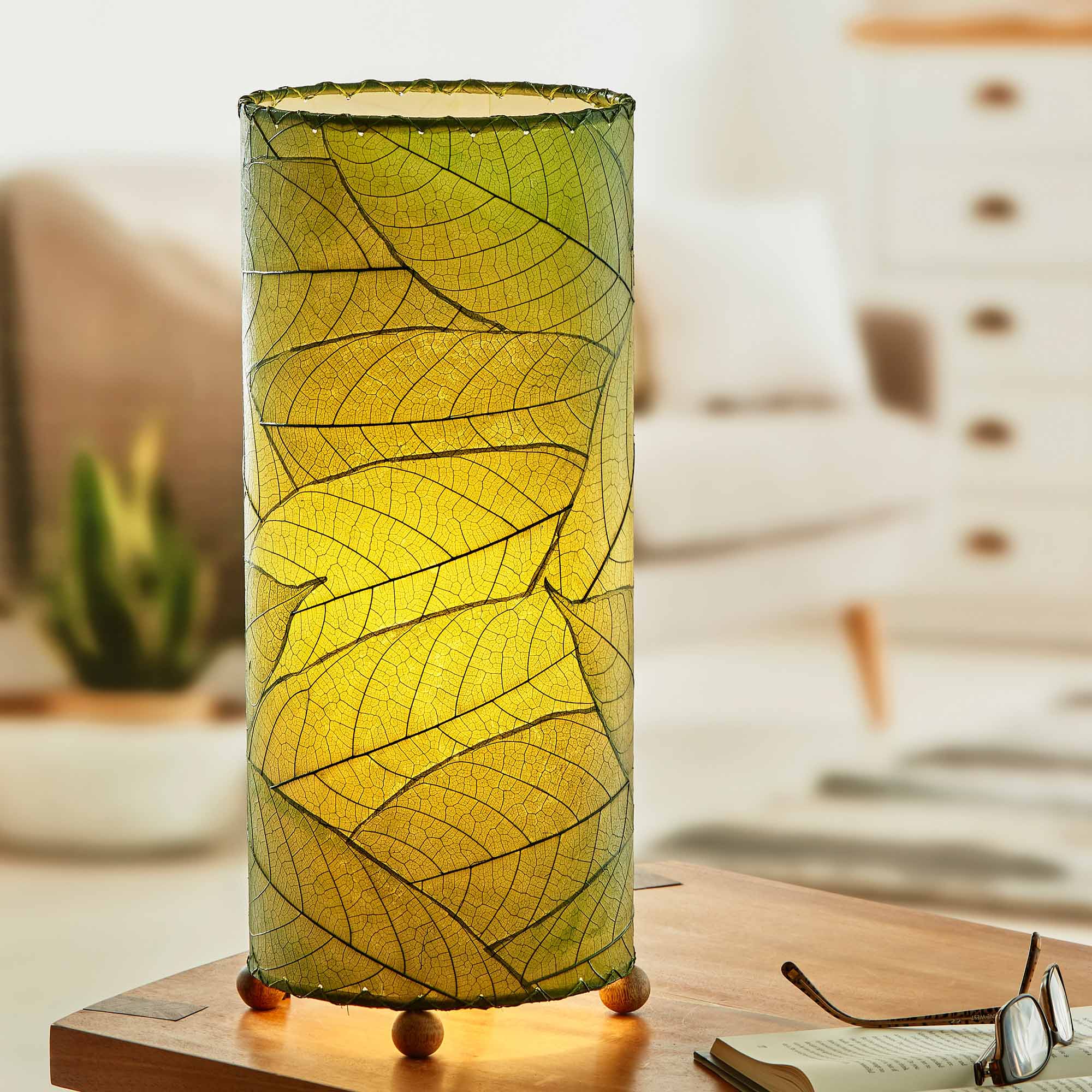 In a quiet bedside corner, crafted by the artisans of Eangee Home Design, the Cocoa Leaf Cylinder Table Lamp in green stands gracefully, featuring fossilized cocoa leaf shade, wrought iron frame, handcrafted, adding warmth and character to the space.