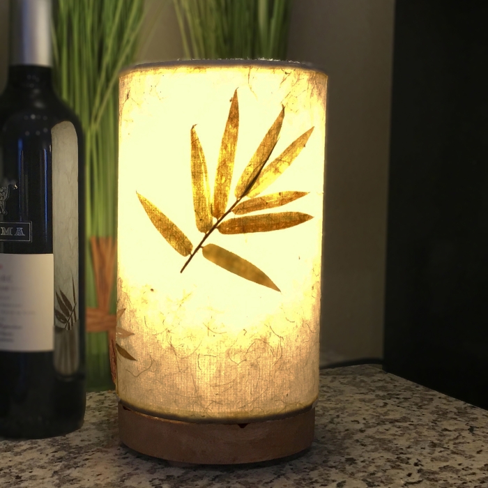 In a coastal inspired living room, crafted by the artisans of Eangee Home Design, the Mini Paper Cylinder Table Lamp Bamboo in natural stands gracefully, featuring reclaimed mango wood base, recycled paper shade, sustainably sourced, recycled materials, adding warmth and character to the space.