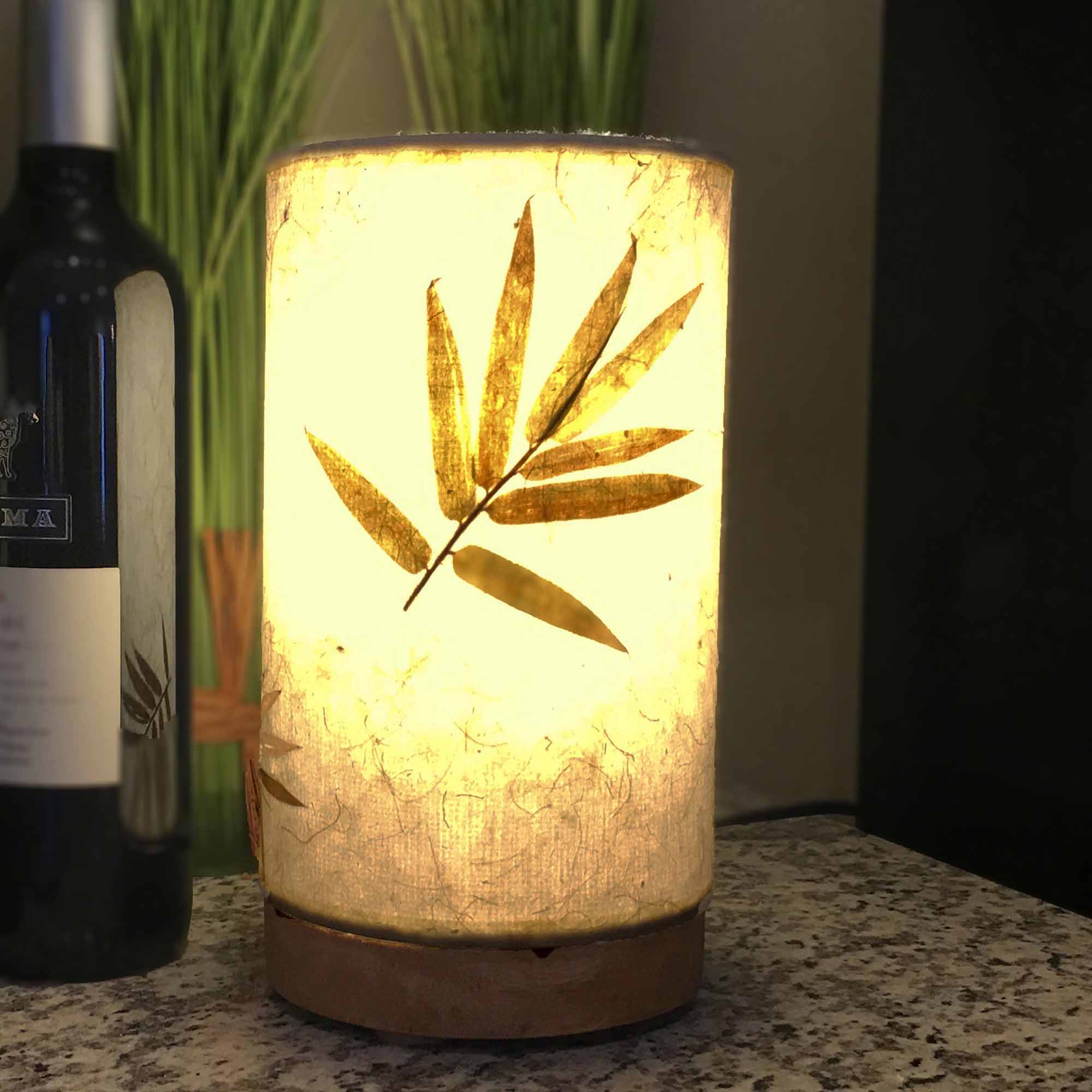 In a coastal inspired living room, crafted by the artisans of Eangee Home Design, the Mini Paper Cylinder Table Lamp Bamboo in natural stands gracefully, featuring reclaimed mango wood base, recycled paper shade, sustainably sourced, recycled materials, adding warmth and character to the space.