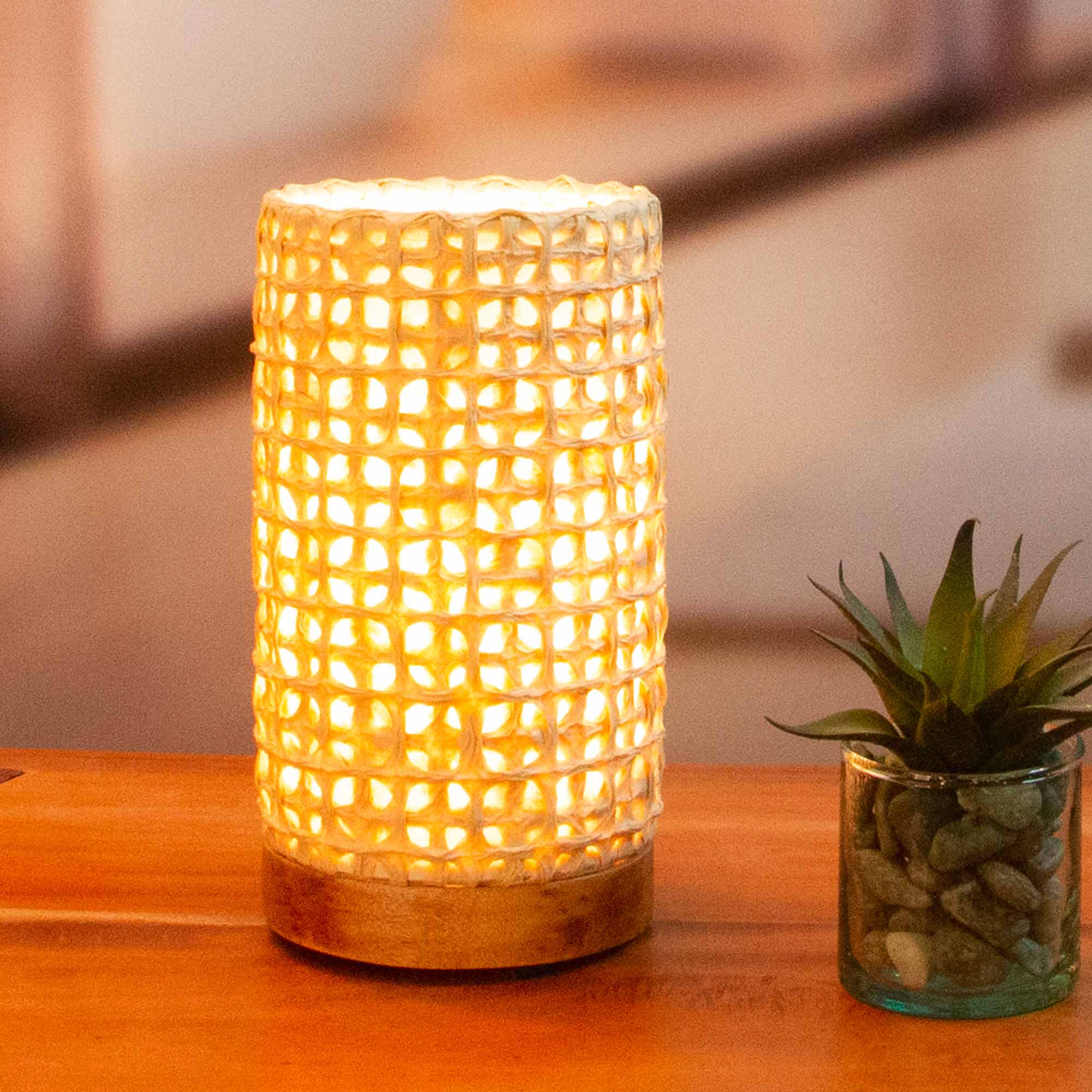 In a minimalist loft with natural textures, crafted by the artisans of Eangee Home Design, the Mini Paper Cylinder Table Lamp Mesh in natural stands gracefully, featuring reclaimed mango wood base, recycled paper shade, sustainably sourced, recycled materials, adding warmth and character to the space.