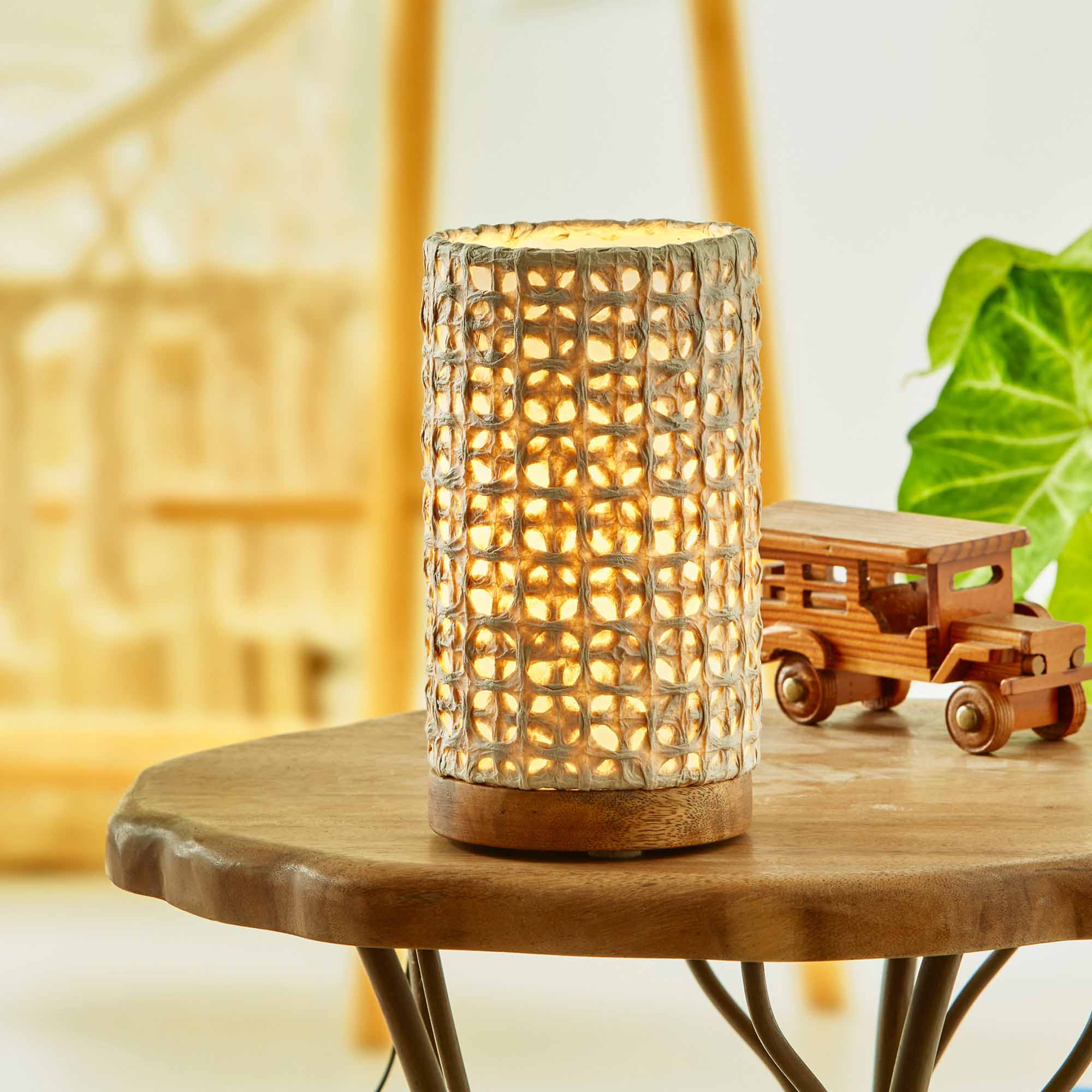 In a sun drenched entryway, crafted by the artisans of Eangee Home Design, the Mini Paper Cylinder Table Lamp Mesh in natural stands gracefully, featuring reclaimed mango wood base, recycled paper shade, sustainably sourced, recycled materials, adding warmth and character to the space.