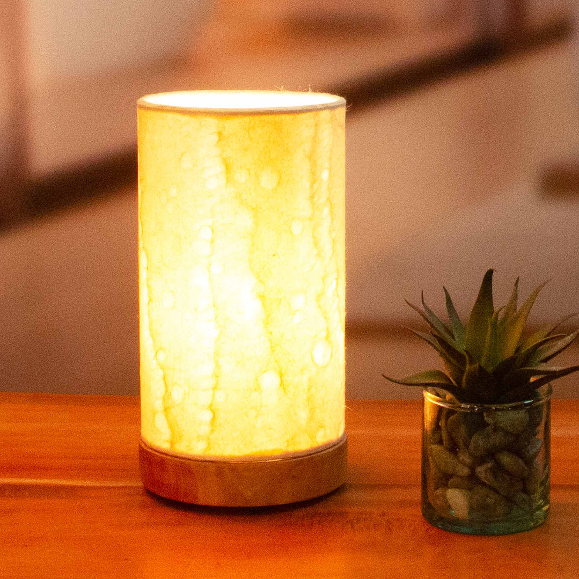 In a sun drenched entryway, crafted by the artisans of Eangee Home Design, the Mini Paper Cylinder Table Lamp Wave in natural stands gracefully, featuring reclaimed mango wood base, recycled paper shade, sustainably sourced, recycled materials, adding warmth and character to the space.