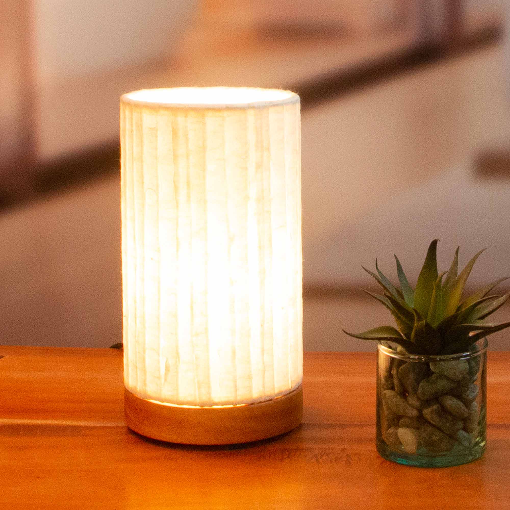In a sun drenched entryway, crafted by the artisans of Eangee Home Design, the Mini Paper Cylinder Table Lamp Lines in natural stands gracefully, featuring reclaimed mango wood base, recycled paper shade, sustainably sourced, recycled materials, adding warmth and character to the space.