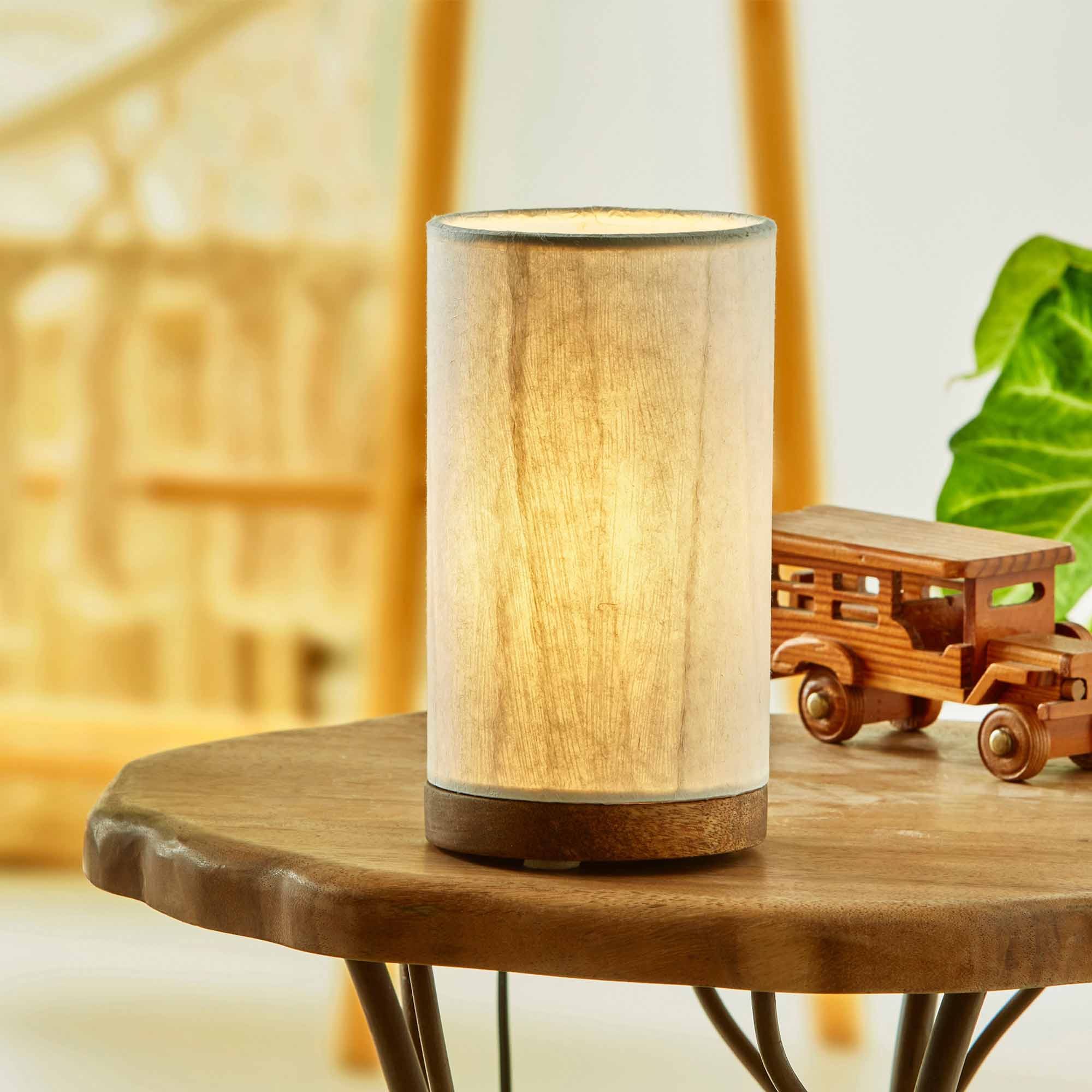 In a sun drenched entryway, crafted by the artisans of Eangee Home Design, the Mini Paper Cylinder Table Lamp Glacier in natural stands gracefully, featuring reclaimed mango wood base, recycled paper shade, sustainably sourced, recycled materials, adding warmth and character to the space.
