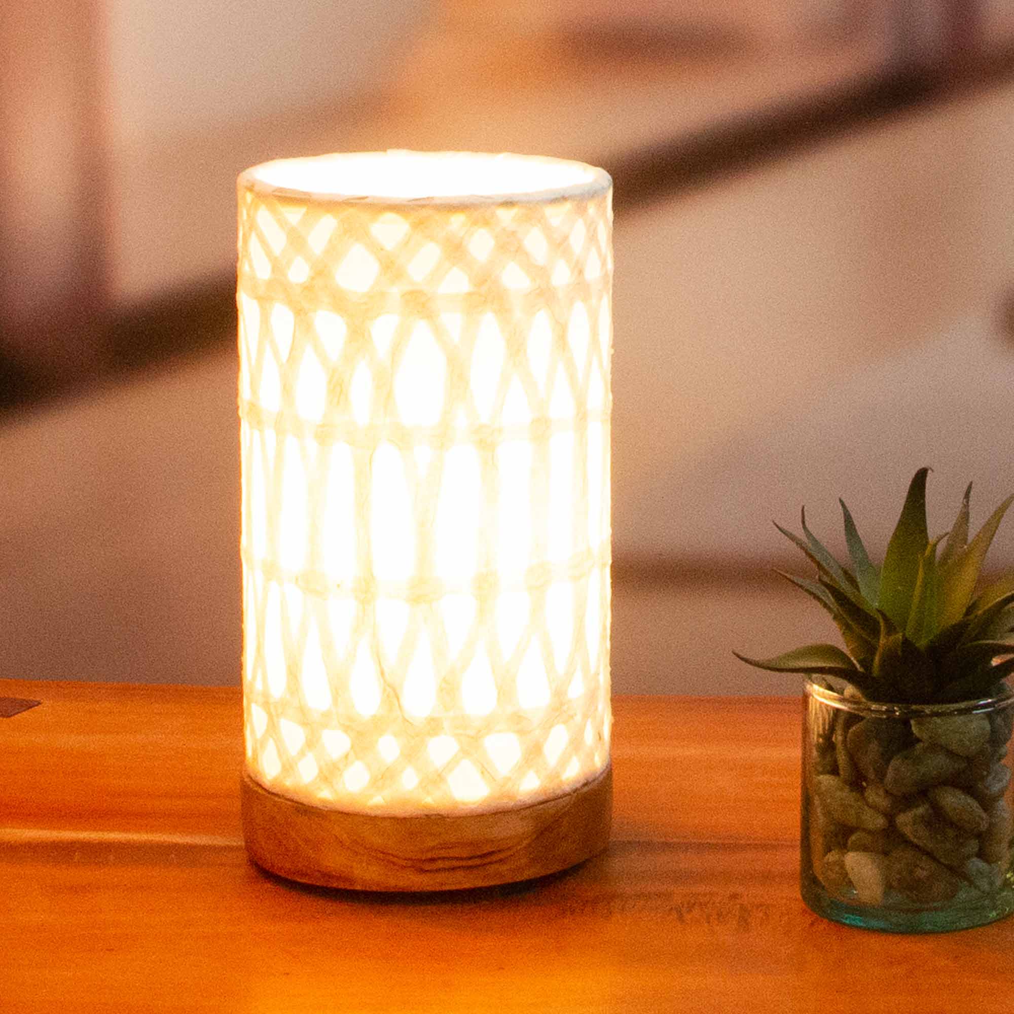 In a quiet bedside corner, crafted by the artisans of Eangee Home Design, the Mini Paper Cylinder Table Lamp Arches in natural stands gracefully, featuring reclaimed mango wood base, recycled paper shade, sustainably sourced, recycled materials, adding warmth and character to the space.
