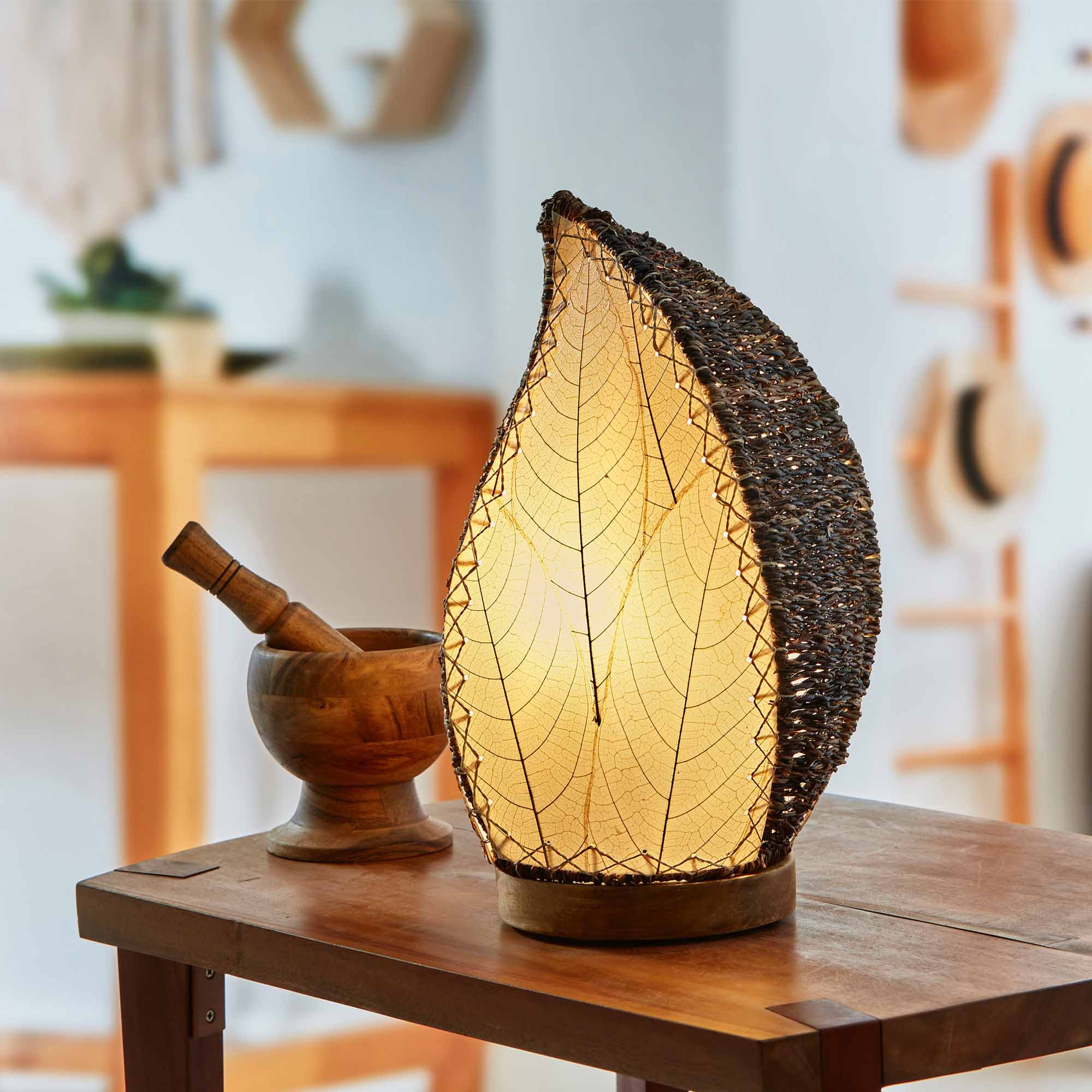 In a modern interior with earth tones, crafted by the artisans of Eangee Home Design, the Leaflet Table Lamp in natural stands gracefully, featuring fossilized cocoa leaf shade, abaca rope accents, reclaimed mango wood base, wrought iron frame, sustainably sourced, adding warmth and character to the space.