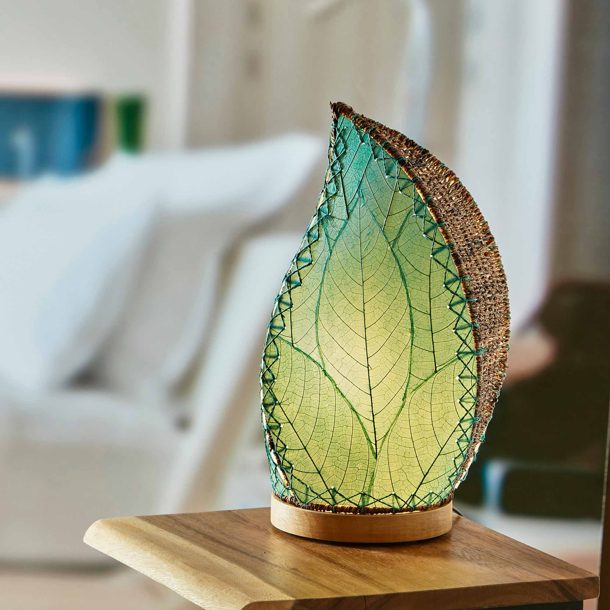 In a sun drenched entryway, crafted by the artisans of Eangee Home Design, the Leaflet Table Lamp in sea blue stands gracefully, featuring fossilized cocoa leaf shade, abaca rope accents, reclaimed mango wood base, wrought iron frame, sustainably sourced, adding warmth and character to the space.