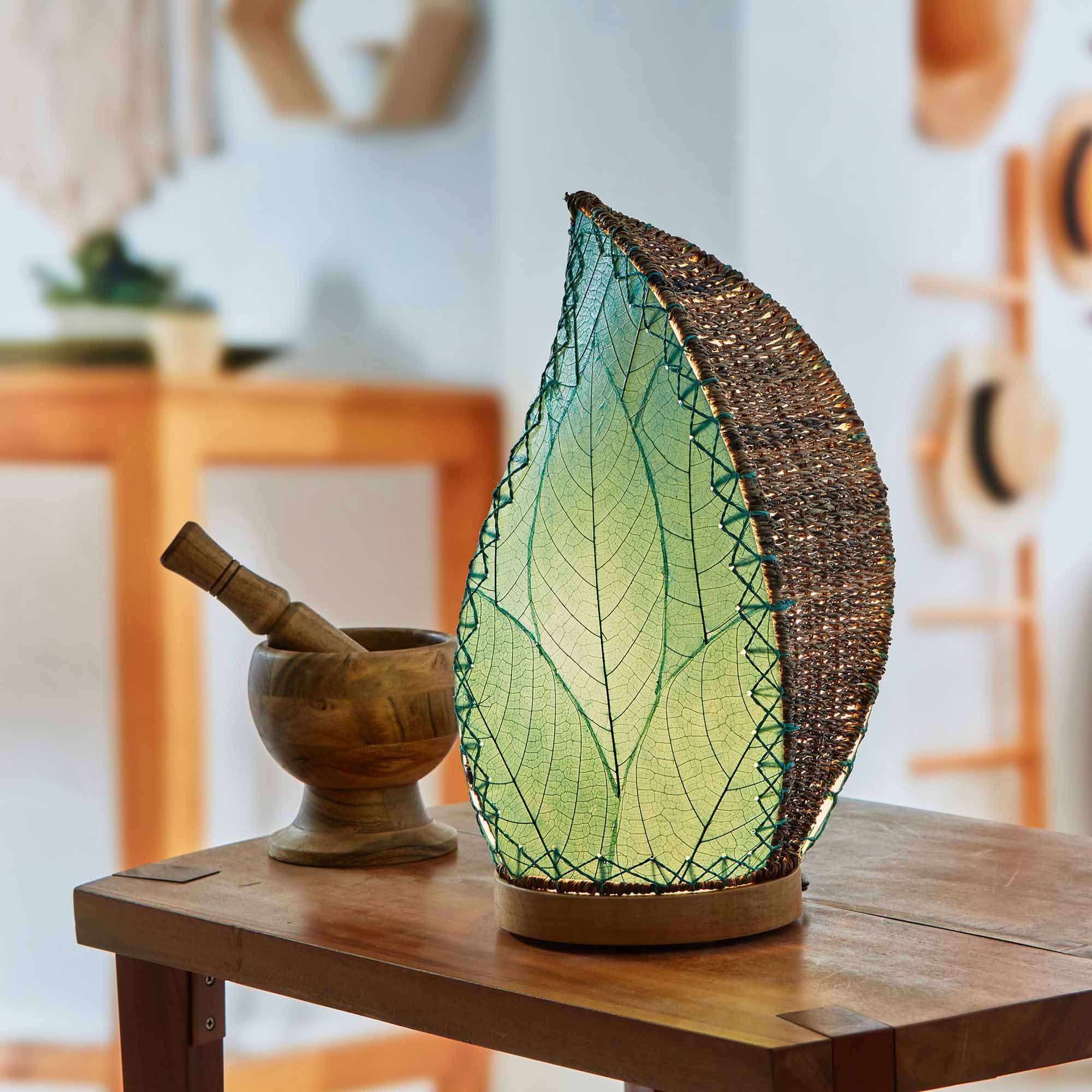 In a modern interior with earth tones, crafted by the artisans of Eangee Home Design, the Leaflet Table Lamp in sea blue stands gracefully, featuring fossilized cocoa leaf shade, abaca rope accents, reclaimed mango wood base, wrought iron frame, sustainably sourced, adding warmth and character to the space.