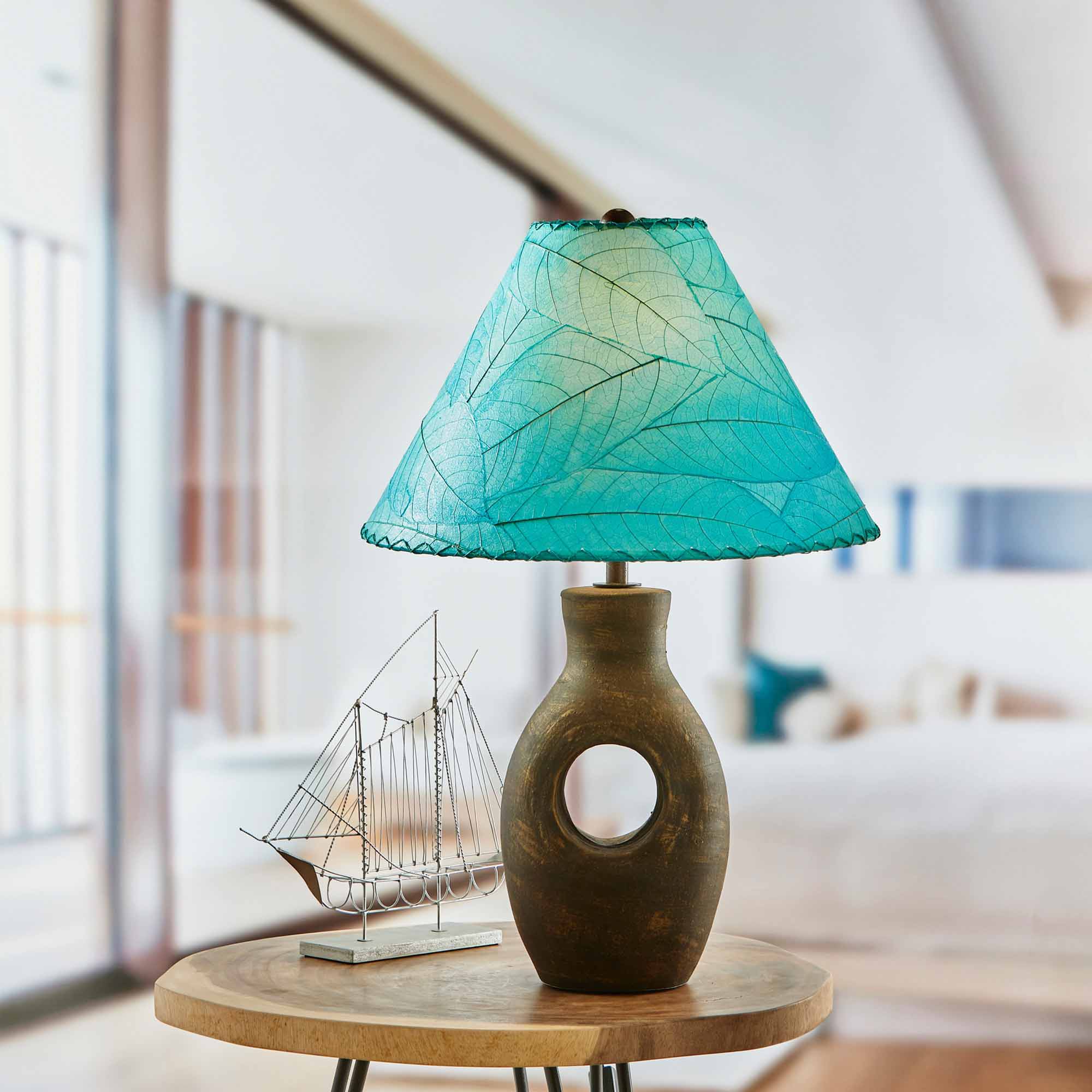 In a softly lit reading nook, crafted by the artisans of Eangee Home Design, the Bell Shade Cocoa in sea blue stands gracefully, featuring fossilized cocoa leaf shade, wrought iron frame, handcrafted, adding warmth and character to the space.