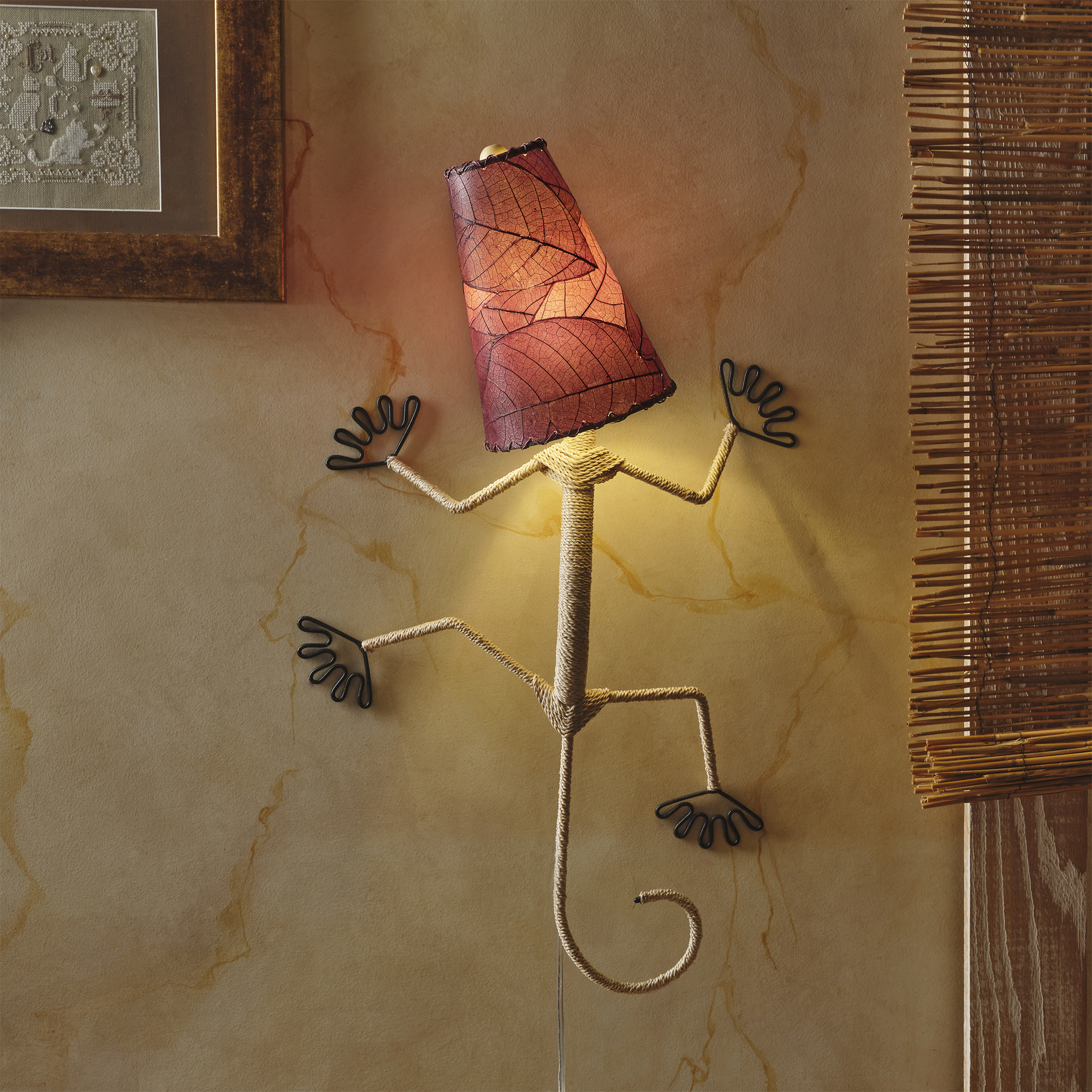 In a softly lit reading nook, crafted by the artisans of Eangee Home Design, the Gecko Wall Lamp Shade in purple hangs, featuring fossilized cocoa leaf shade, abaca rope accents, wrought iron frame, handcrafted, adding warmth and character to the space.