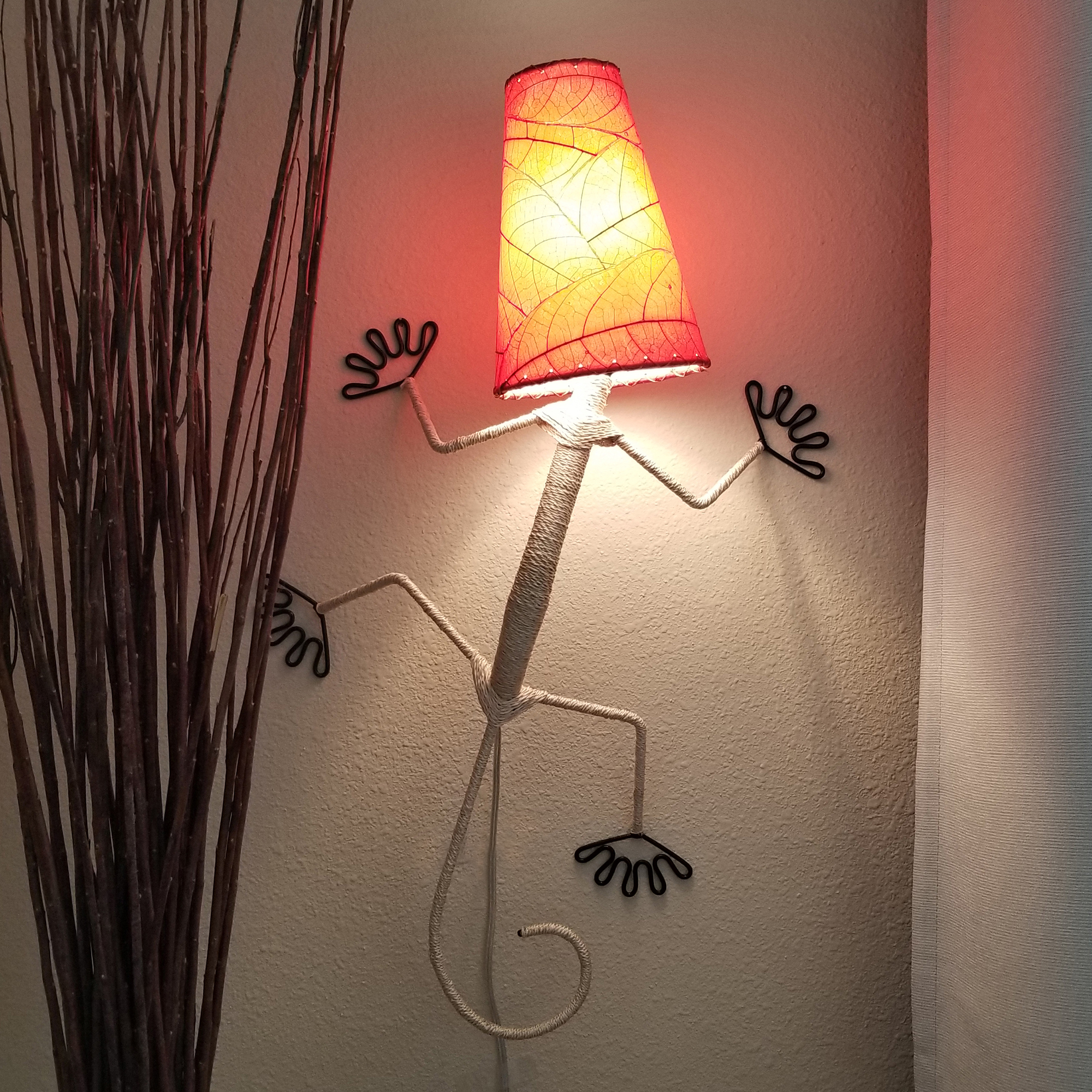 In a coastal inspired living room, crafted by the artisans of Eangee Home Design, the Gecko Wall Lamp Shade in red hangs, featuring fossilized cocoa leaf shade, abaca rope accents, wrought iron frame, handcrafted, adding warmth and character to the space.