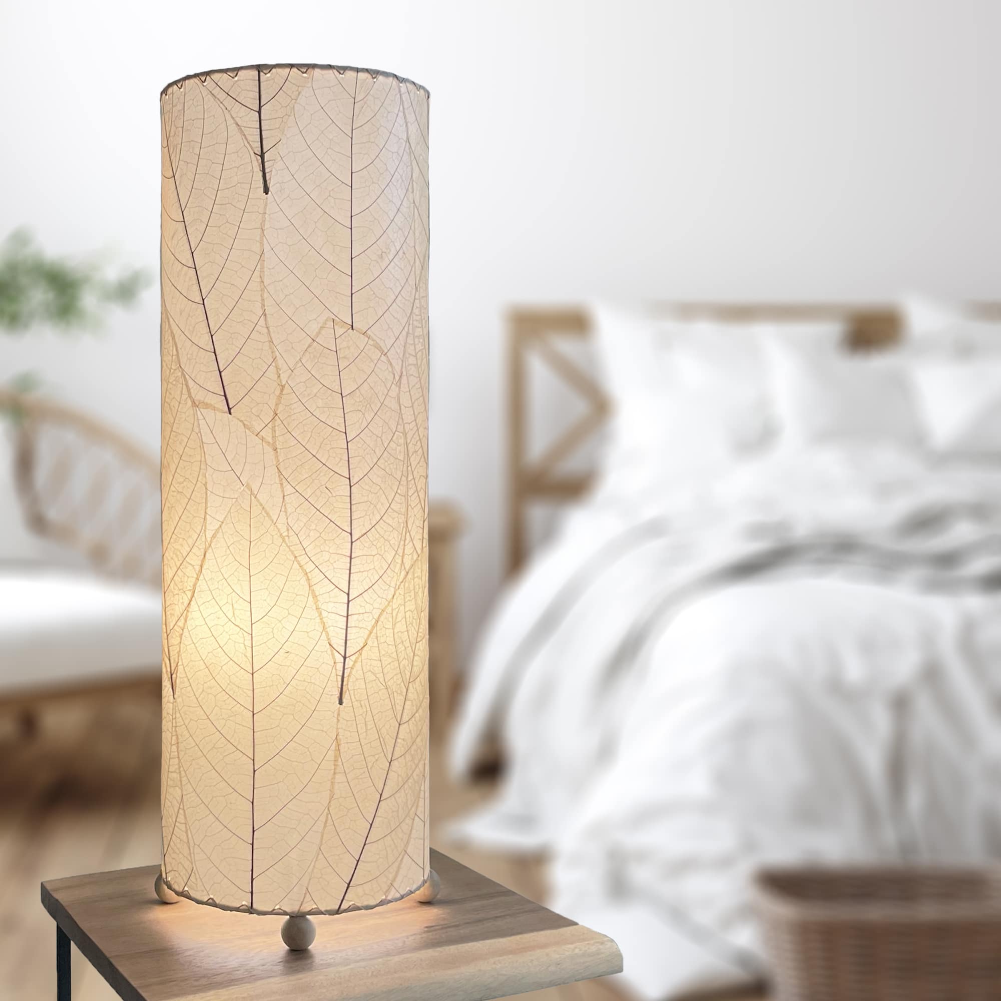 In a sun drenched entryway, crafted by the artisans of Eangee Home Design, the 24 Inch Cocoa Leaf Cylinder Table Lamp in natural stands gracefully, featuring fossilized cocoa leaf shade, fair trade, eco friendly, sustainably sourced, handcrafted, adding warmth and character to the space.
