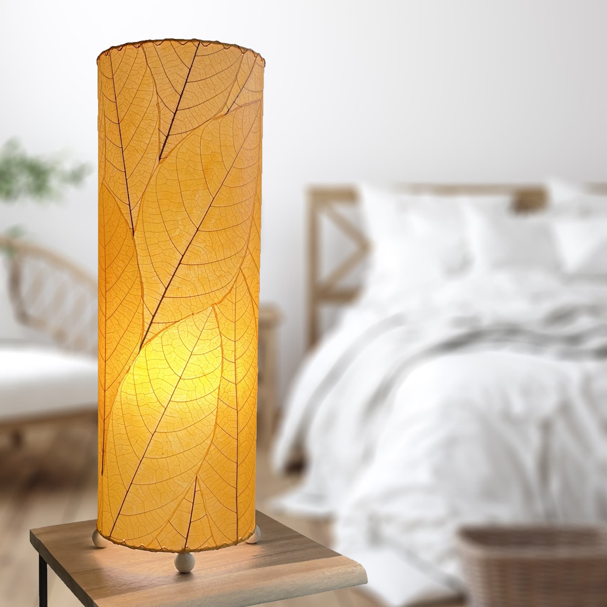 In a modern interior with earth tones, crafted by the artisans of Eangee Home Design, the 24 Inch Cocoa Leaf Cylinder Table Lamp in orange stands gracefully, featuring fossilized cocoa leaf shade, fair trade, eco friendly, sustainably sourced, handcrafted, adding warmth and character to the space.