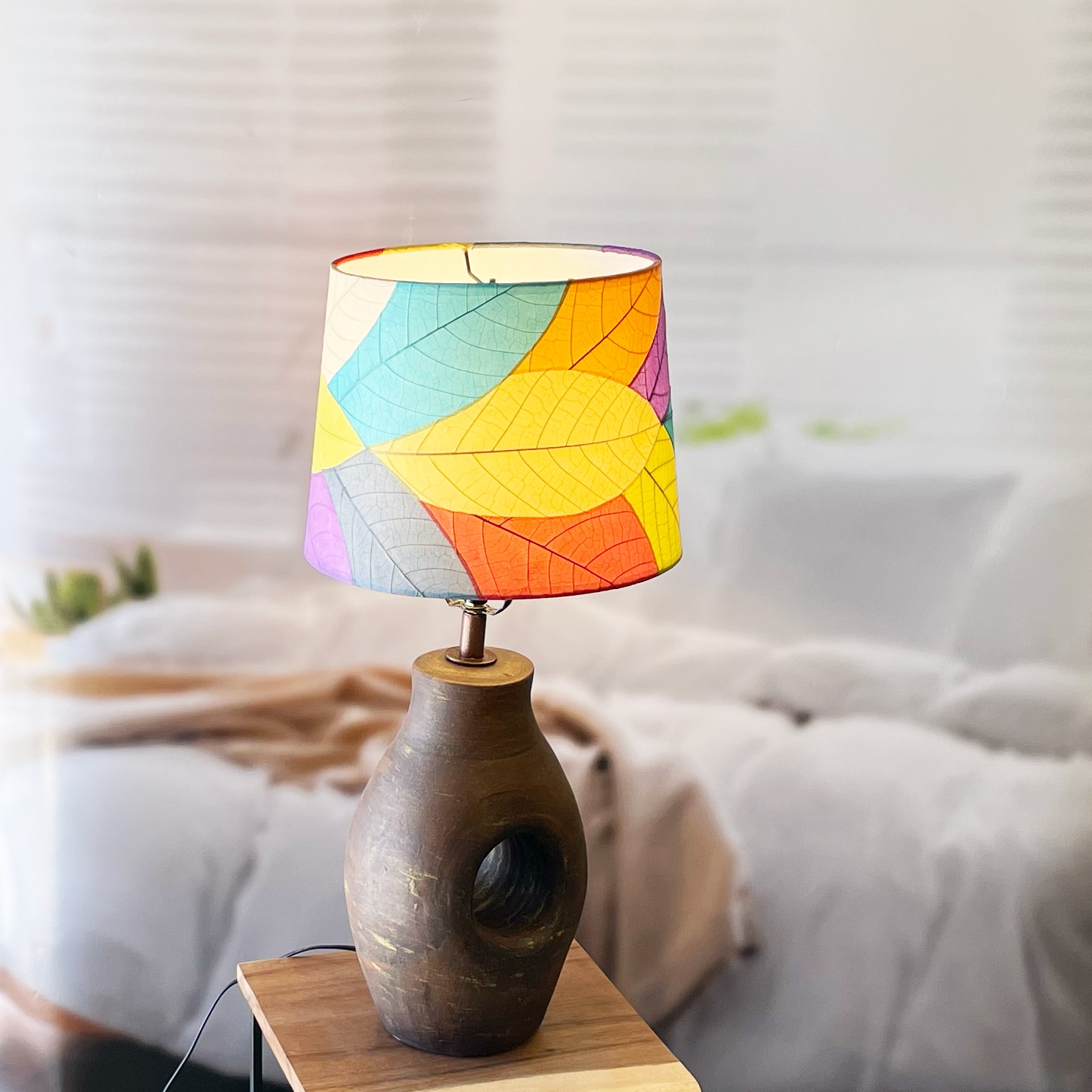 In a softly lit reading nook, crafted by the artisans of Eangee Home Design, the 12 Inch Tapered Drum Shade in multi color stands gracefully, featuring fossilized cocoa leaf shade, fair trade, adding warmth and character to the space.