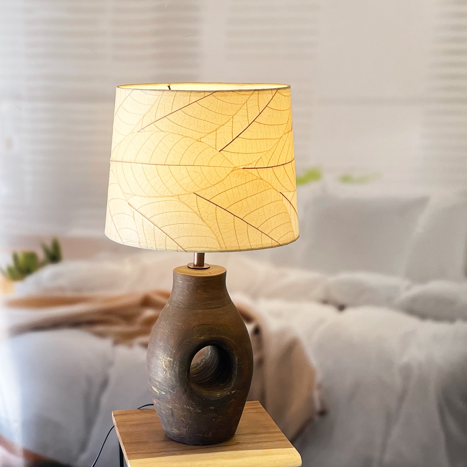 In a sun drenched entryway, crafted by the artisans of Eangee Home Design, the 14 Inch Tapered Drum Shade in natural stands gracefully, featuring fossilized cocoa leaf shade, wrought iron frame, fair trade, eco friendly, sustainably sourced, handcrafted, adding warmth and character to the space.