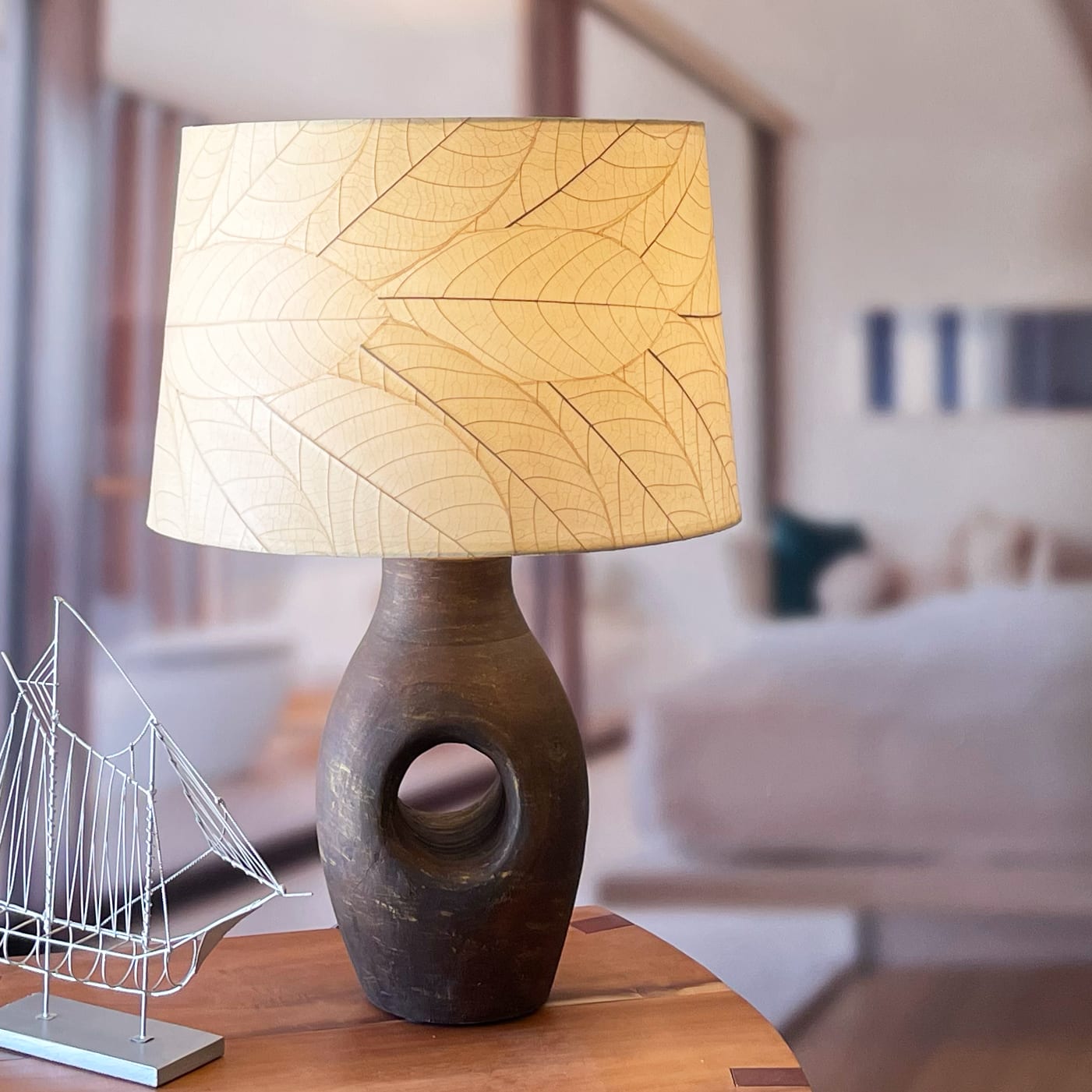 In a sun drenched entryway, crafted by the artisans of Eangee Home Design, the 18 Inch Tapered Drum Shade in natural stands gracefully, featuring fossilized cocoa leaf shade, wrought iron frame, eco friendly, sustainably sourced, adding warmth and character to the space.
