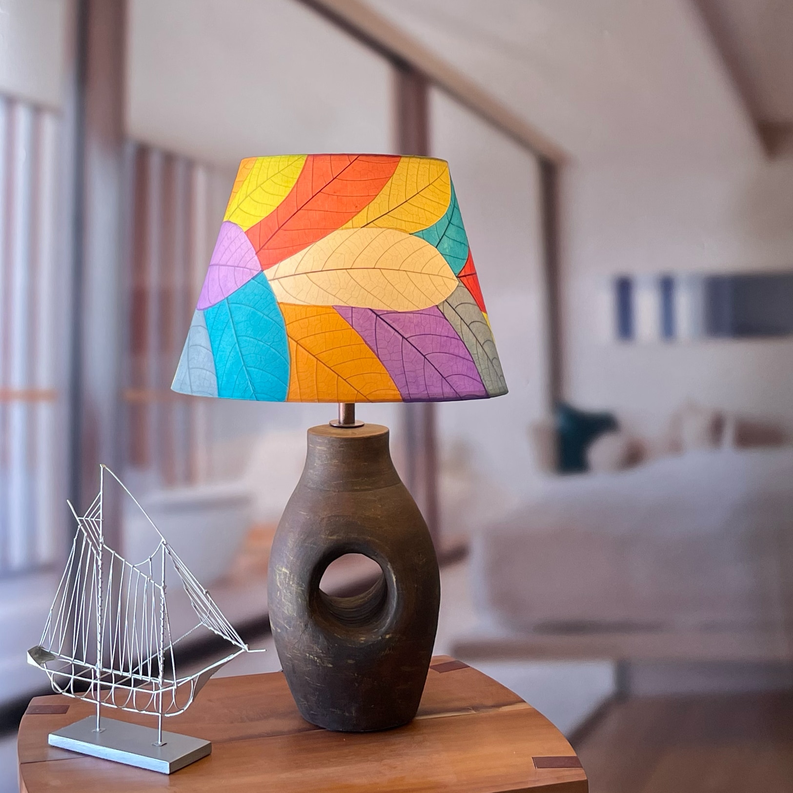 In a modern interior with earth tones, crafted by the artisans of Eangee Home Design, the 16 Inch British Empire Shade in multi color stands gracefully, featuring fossilized cocoa leaf shade, wrought iron frame, fair trade, eco friendly, sustainably sourced, adding warmth and character to the space.