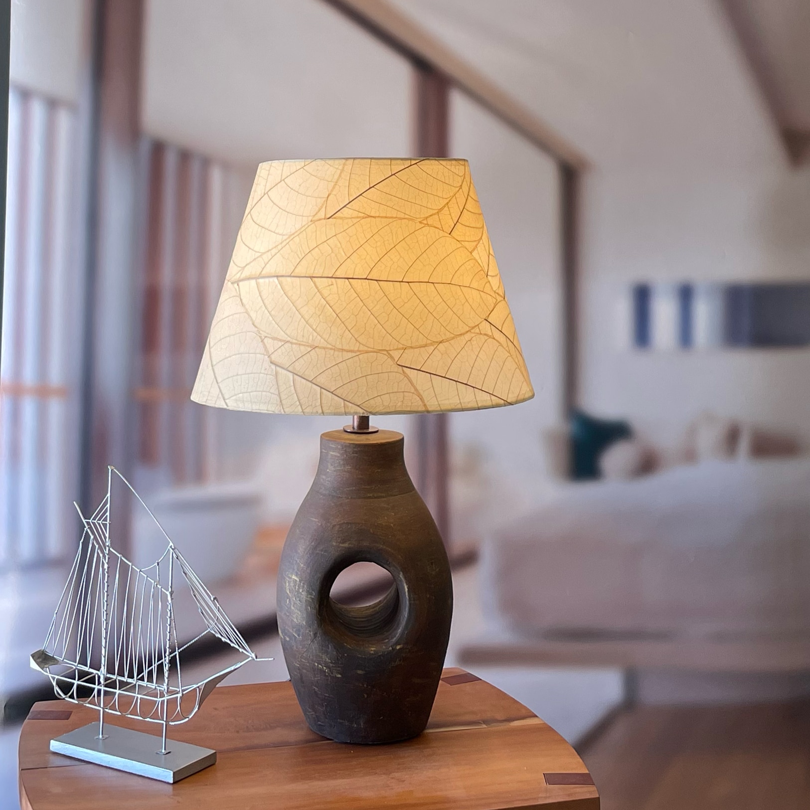 In a minimalist loft with natural textures, crafted by the artisans of Eangee Home Design, the 16 Inch British Empire Shade in natural stands gracefully, featuring fossilized cocoa leaf shade, wrought iron frame, fair trade, eco friendly, sustainably sourced, adding warmth and character to the space.