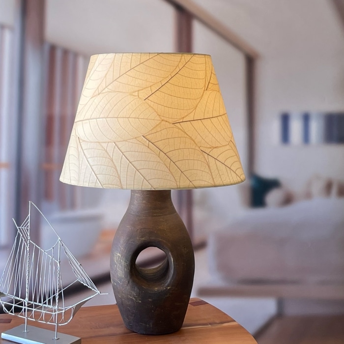 In a softly lit reading nook, crafted by the artisans of Eangee Home Design, the 18 Inch British Empire Shade in natural stands gracefully, featuring fossilized cocoa leaf shade, wrought iron frame, eco friendly, sustainably sourced, adding warmth and character to the space.
